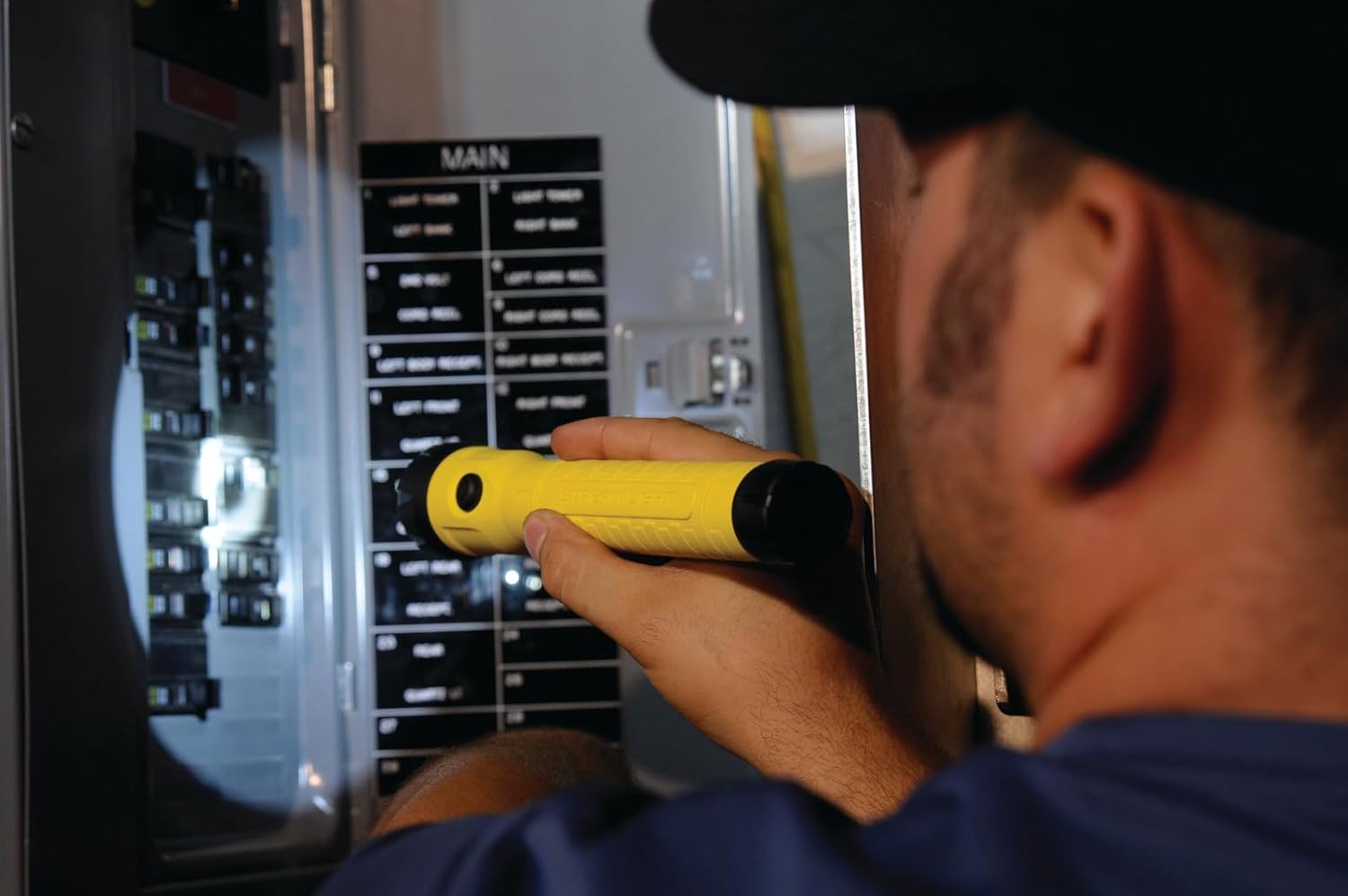 Person using a yellow Streamlight PolyStinger LED HAZ-LO flashlight to inspect an electrical panel.