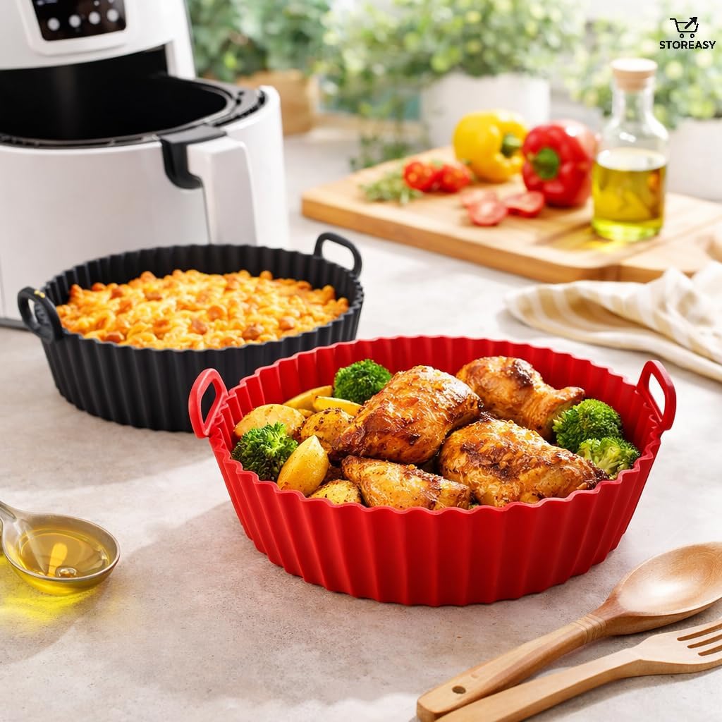 Cena de cozinha iluminada mostrando dois cestos de silicone para air fryer: um vermelho em destaque com sobrecoxas de frango assadas, batatas e brócolis, e um preto ao fundo com macarrão gratinado. Ao lado, uma air fryer branca, colheres de madeira e legumes frescos sobre uma tábua, reforçando a praticidade do preparo.