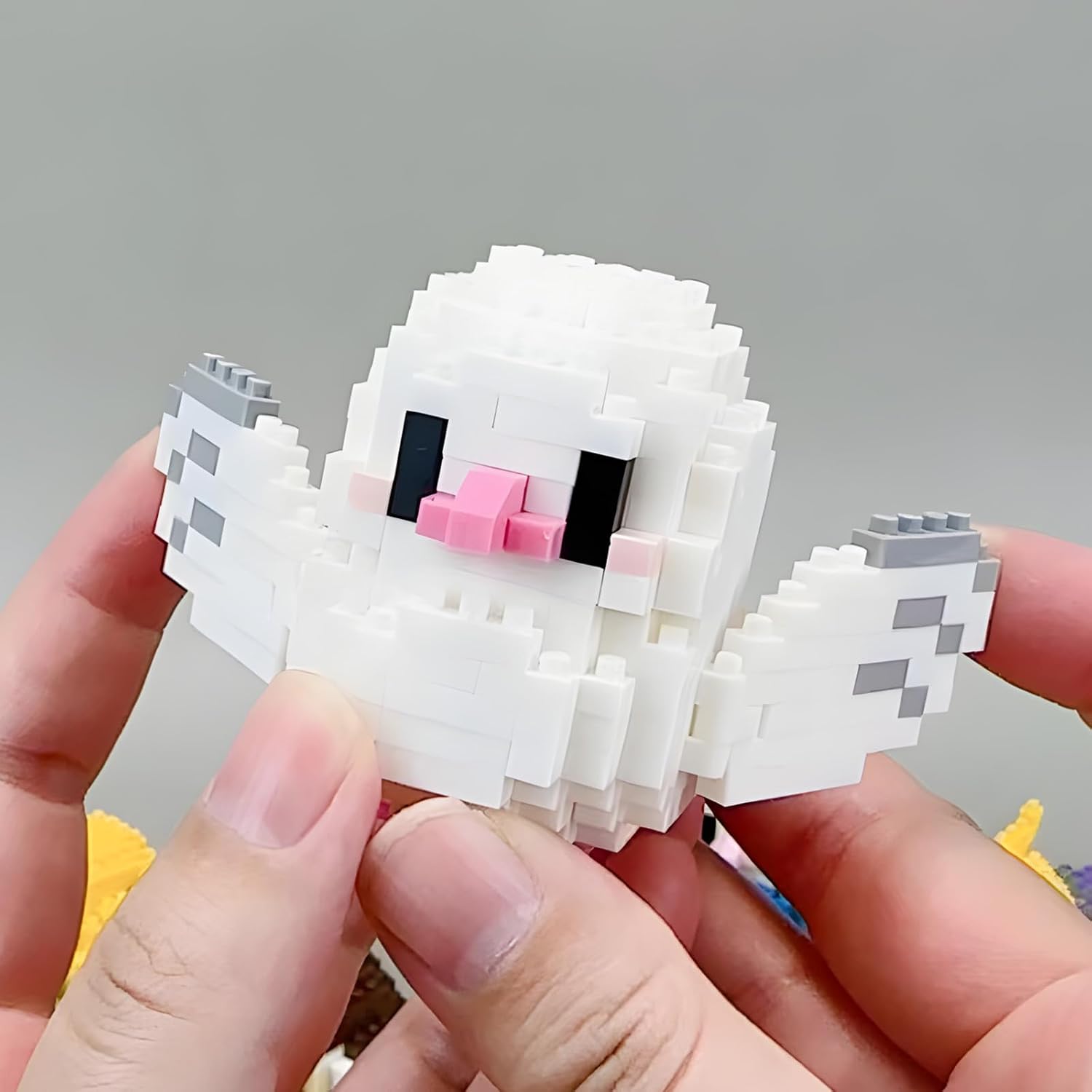 Hands holding a partially assembled white parrot micro building block model.