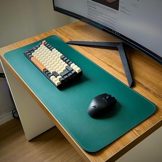 Mouse pad verde grande em uso em uma mesa de madeira com teclado e monitor.