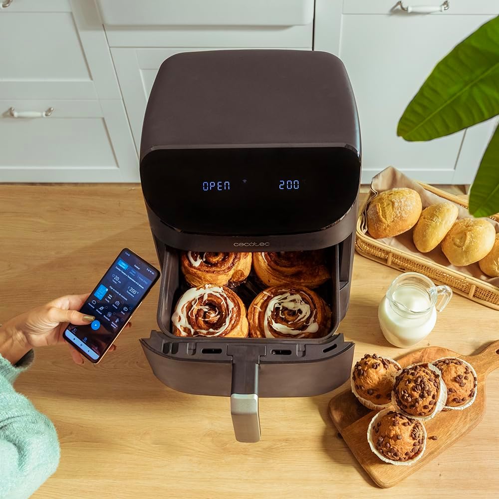 A person controlling the Cecotec Cecofry FoodCourt 11000 Connected C. with a smartphone app, with cinnamon rolls in the oven.