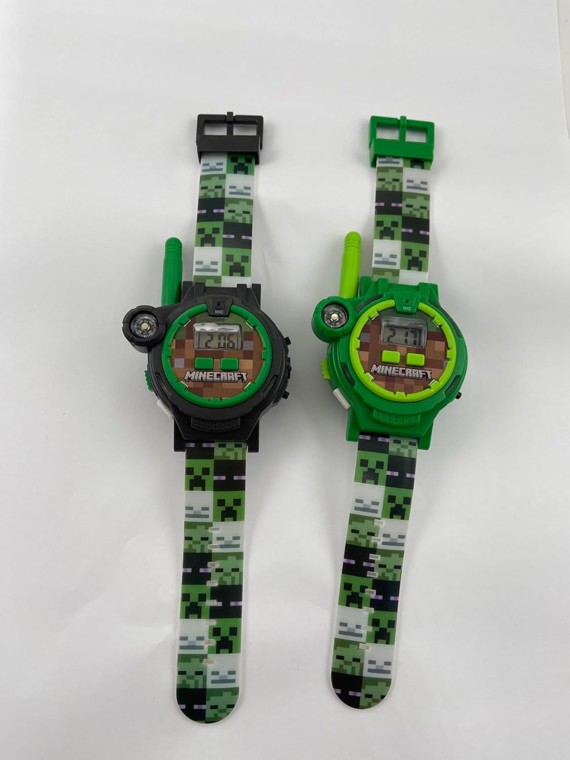 Back view of two Minecraft Walkie Talkie Watches, one black and one green, showing the battery compartment and regulatory information.