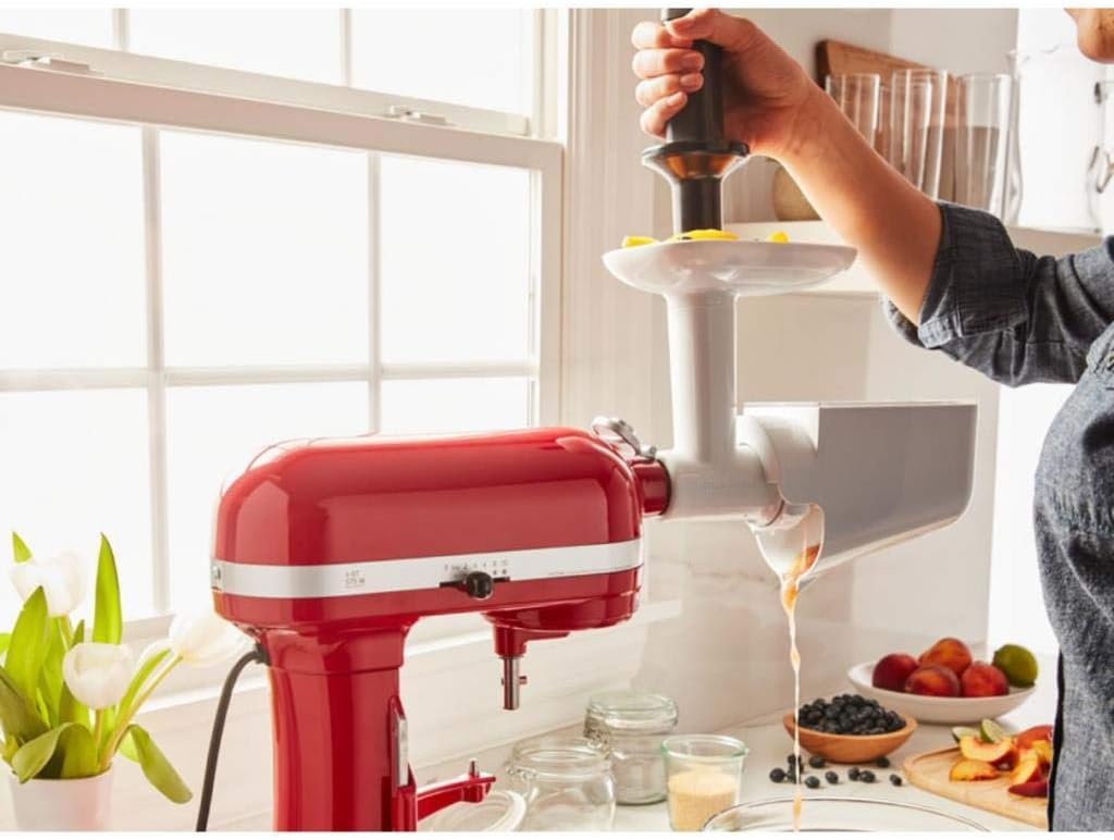 A person using the KitchenAid Fruit and Vegetable Strainer attachment on a red stand mixer, processing fruit into a bowl