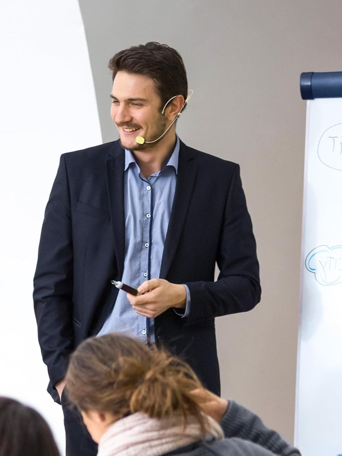 A man presenting in a classroom or conference setting, wearing a headset microphone.