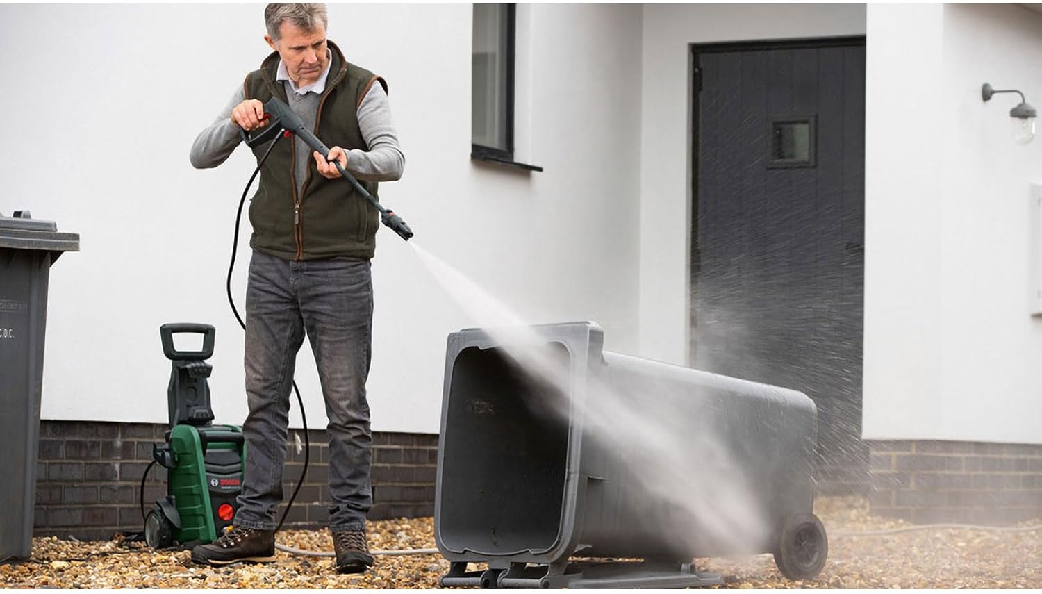 Man cleaning a large waste bin with the Bosch pressure washer