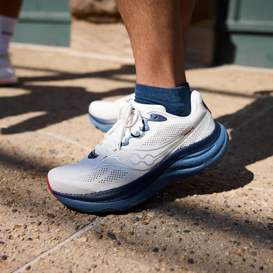 Runner wearing a white and blue cushioned daily running shoe on pavement