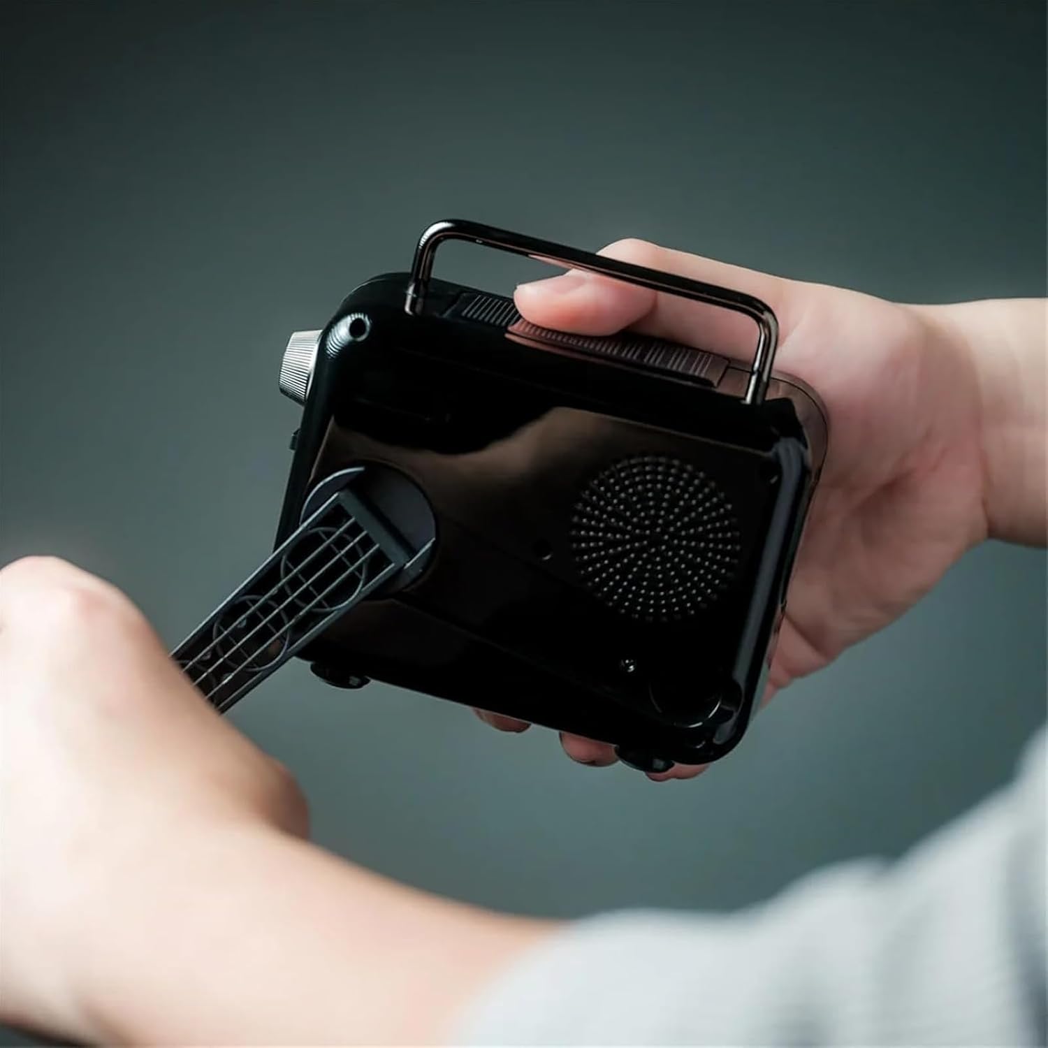 Hands operating the hand crank on the back of the black Retrowave 7-in-1 Portable Radio.