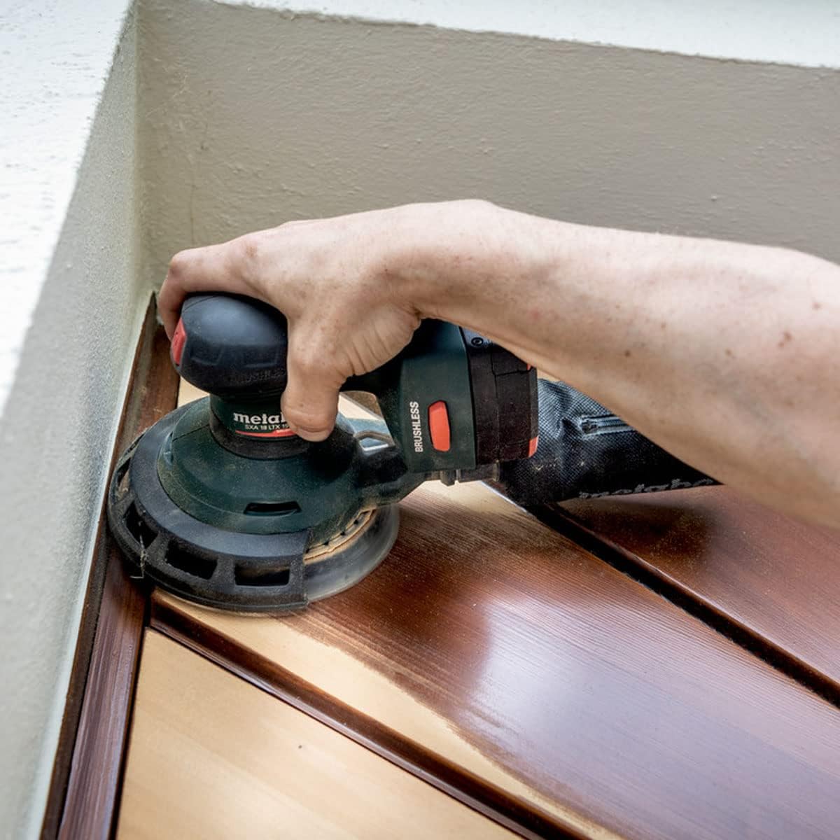 Hand operating Metabo sander on a wooden surface