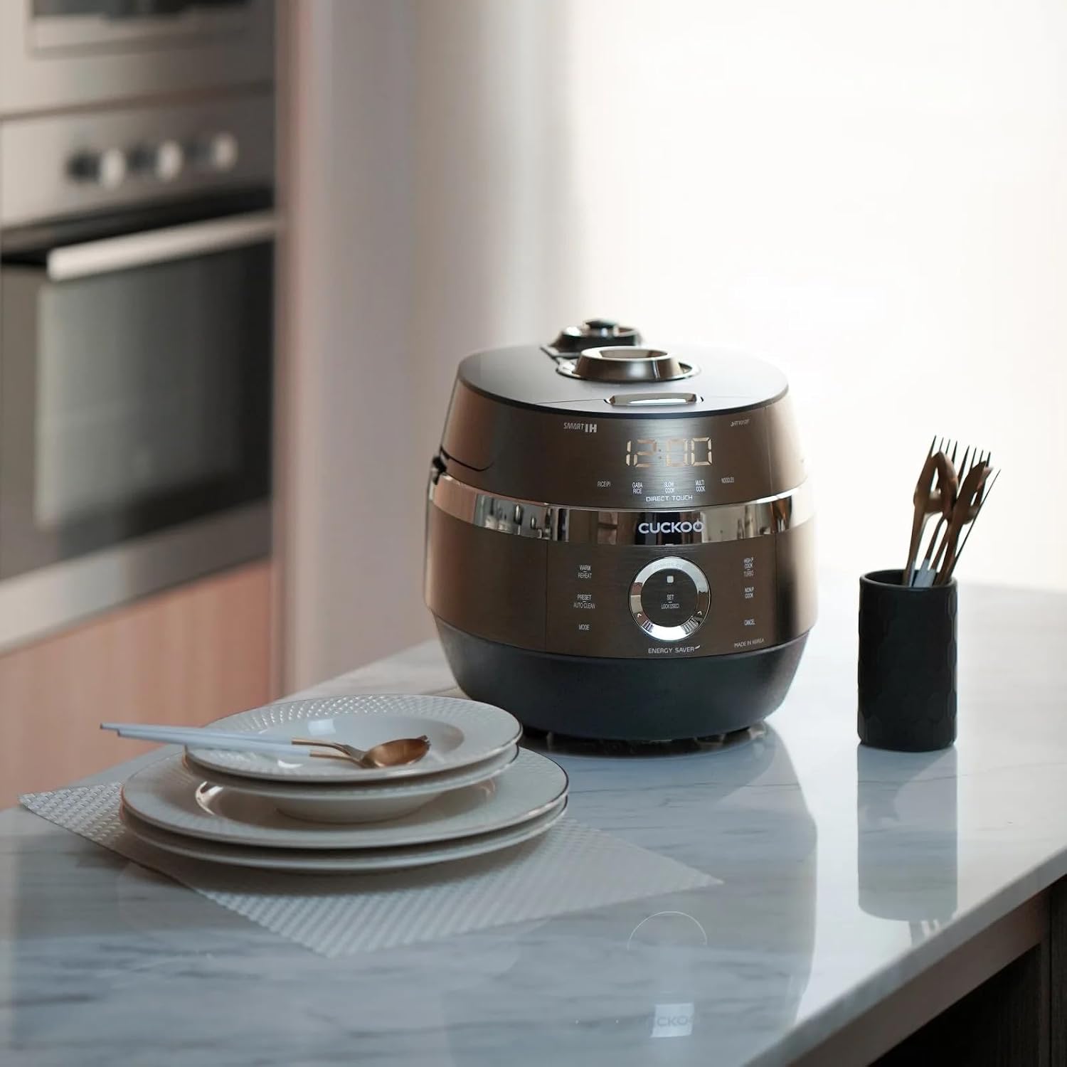 CUCKOO CRP-JHT1012F Twin Pressure Multi-Cooker on a kitchen counter next to plates and cutlery.