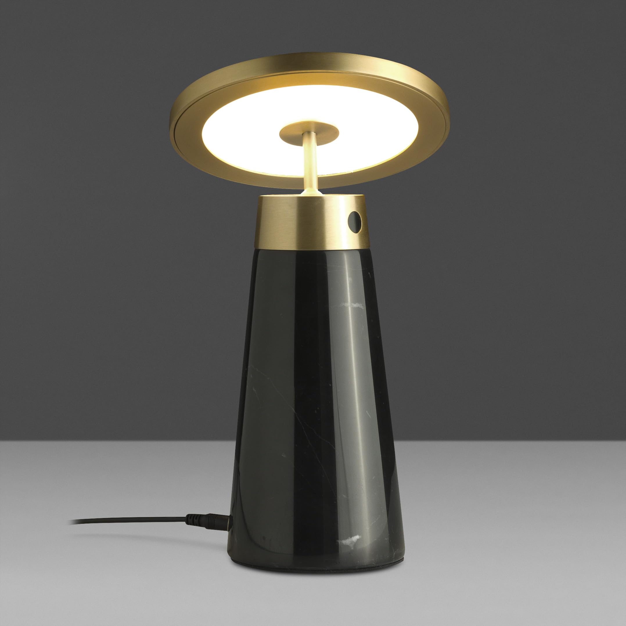 Lámpara de sobremesa con cuerpo de mármol porcelánico similar nero marquina y disco direccional de acero pulido dorado. Dispone de dimmer regulable en intensidad y color