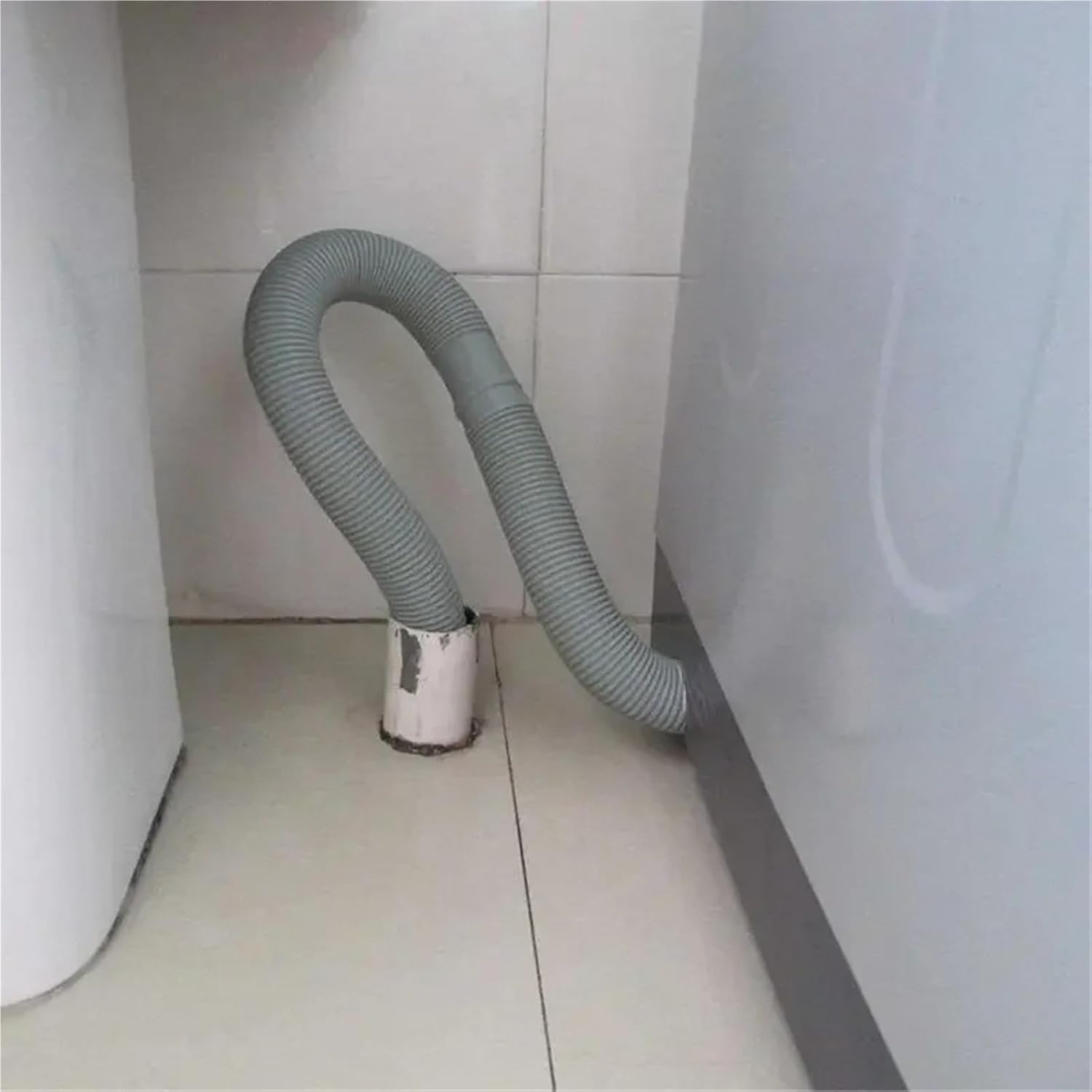 Drain hose curved into a floor drain next to an appliance.