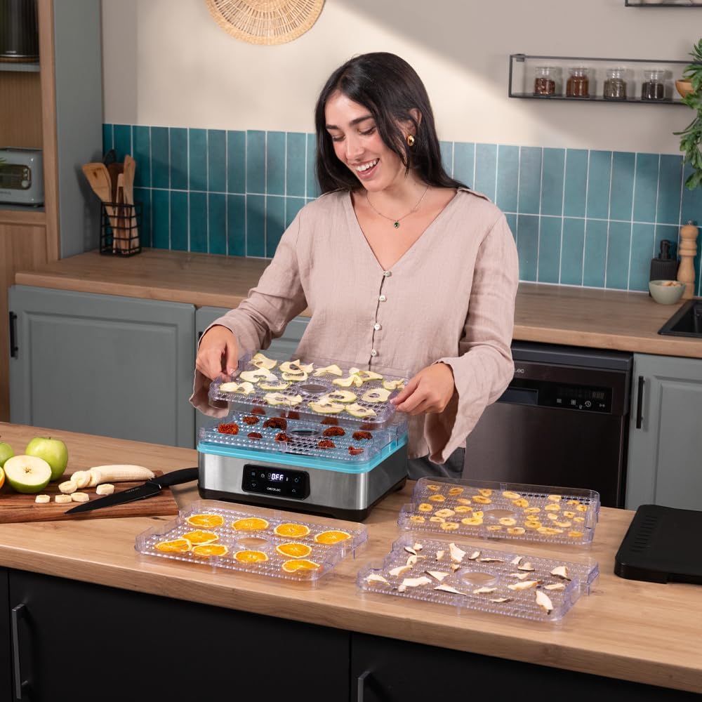 A person placing a tray filled with sliced apples and other fruits into the Cecotec VitaDry Pro Food Dehydrator.