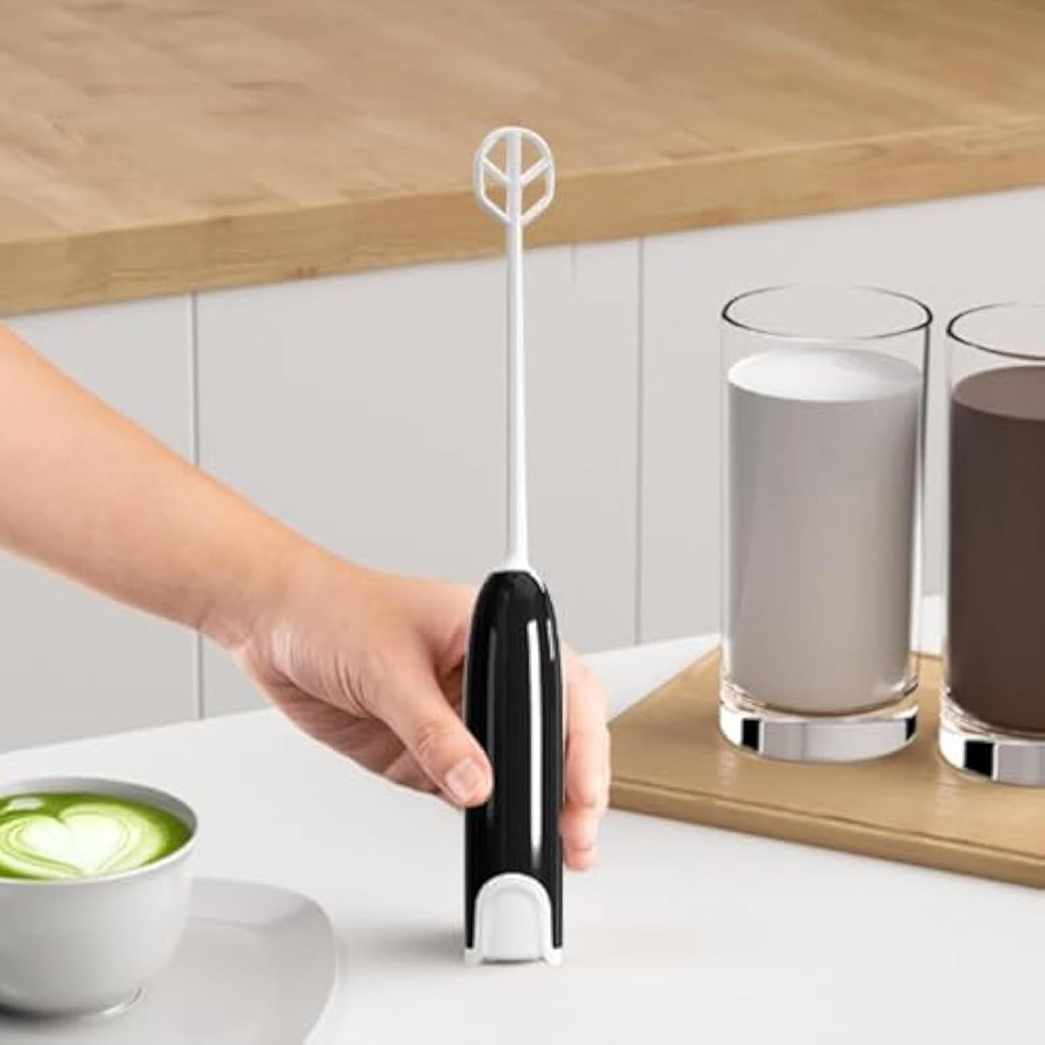 Hand holding the Handheld Electric Beverage Mixer next to two glasses of drinks