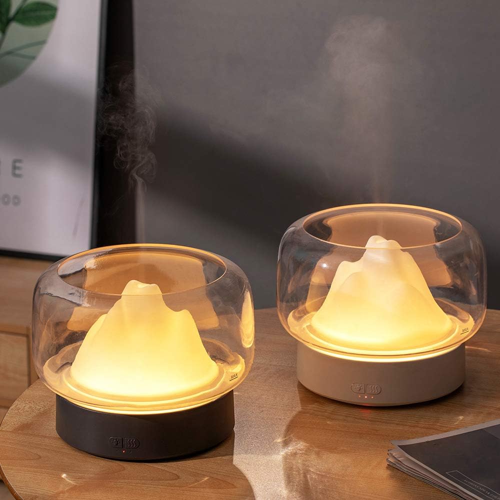 Two Premium Aromatherapy Diffusers, one with a dark base and one with a light base, both emitting warm light, placed on a wooden surface.