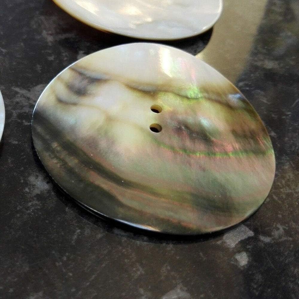 A close-up of a large mother of pearl button with a strong iridescent green and pink sheen.
