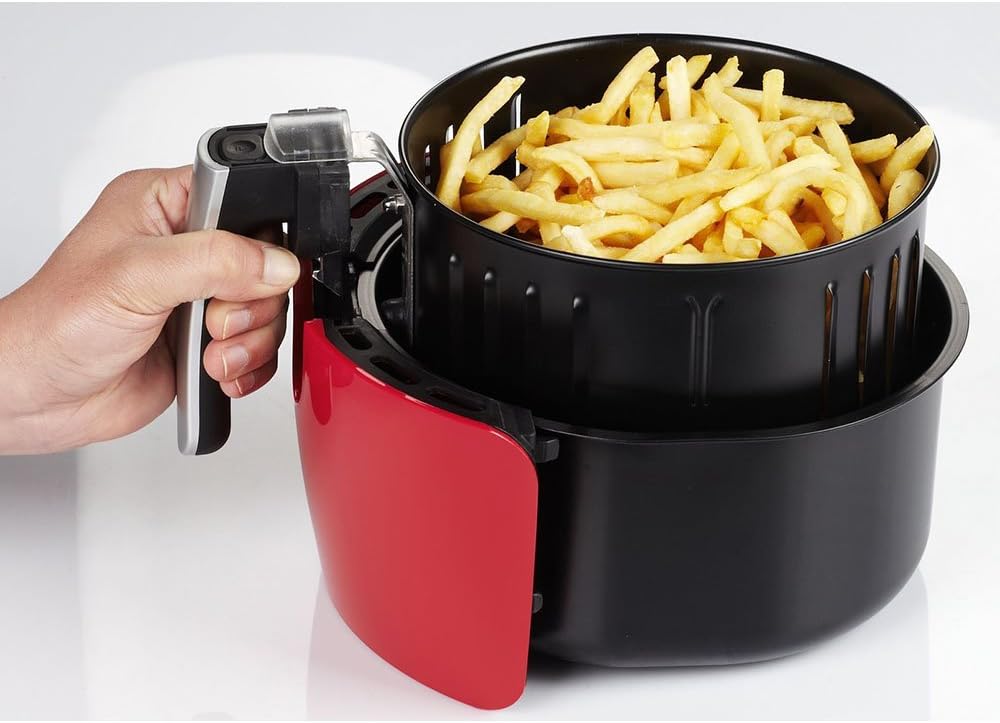 Close-up of a hand holding the air fryer basket filled with french fries, detached from the main unit.