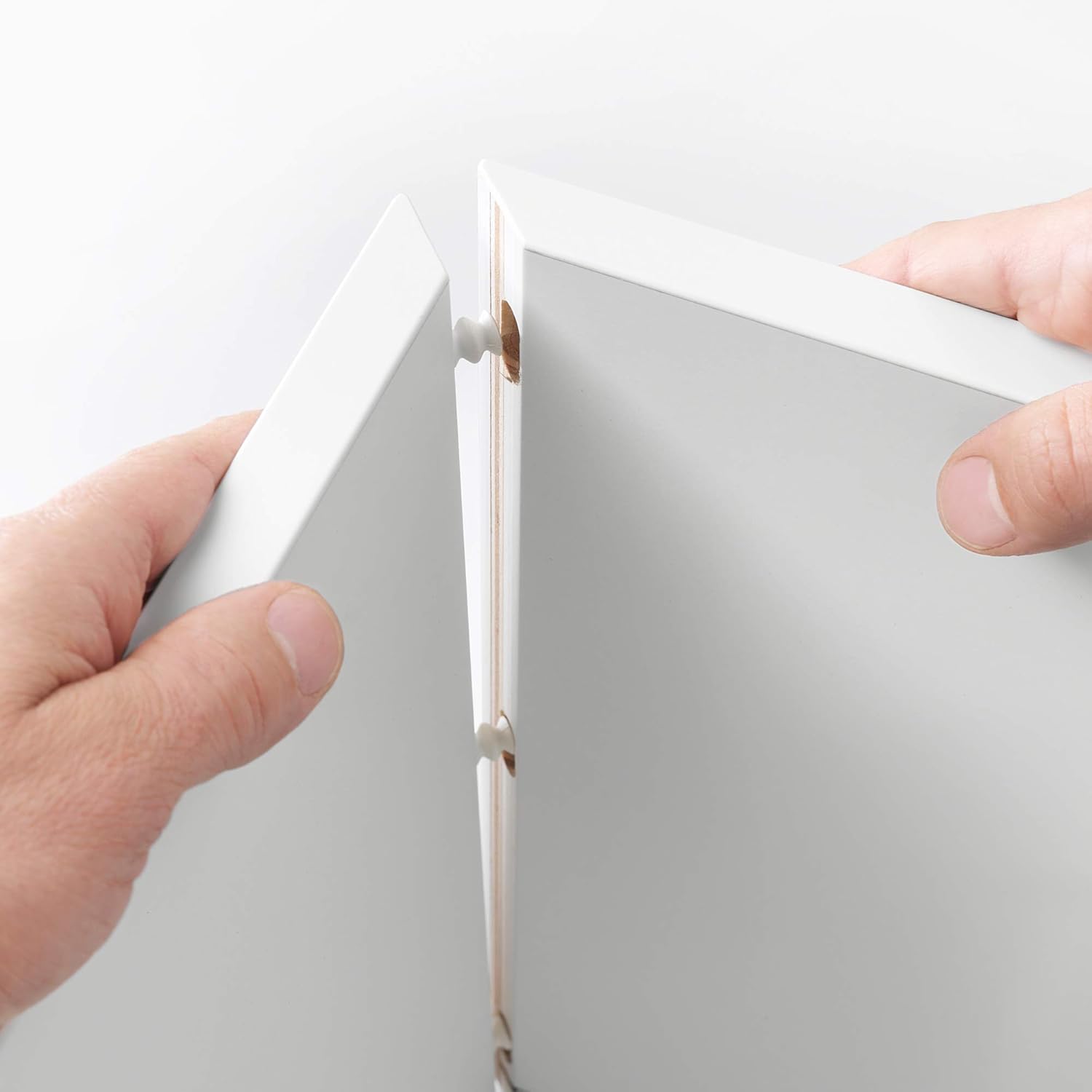 Hands connecting two white furniture panels with a wedge dowel