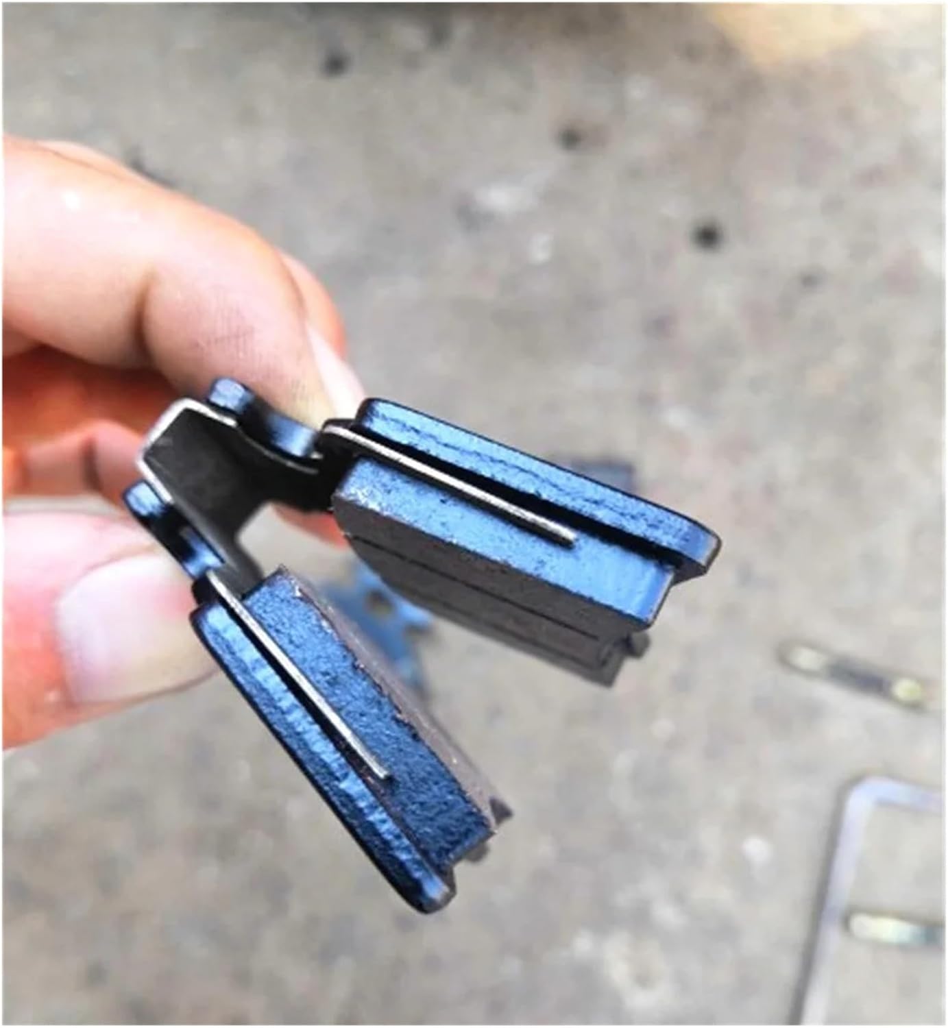 Hand holding two brake pads, showing the spring clip mechanism.