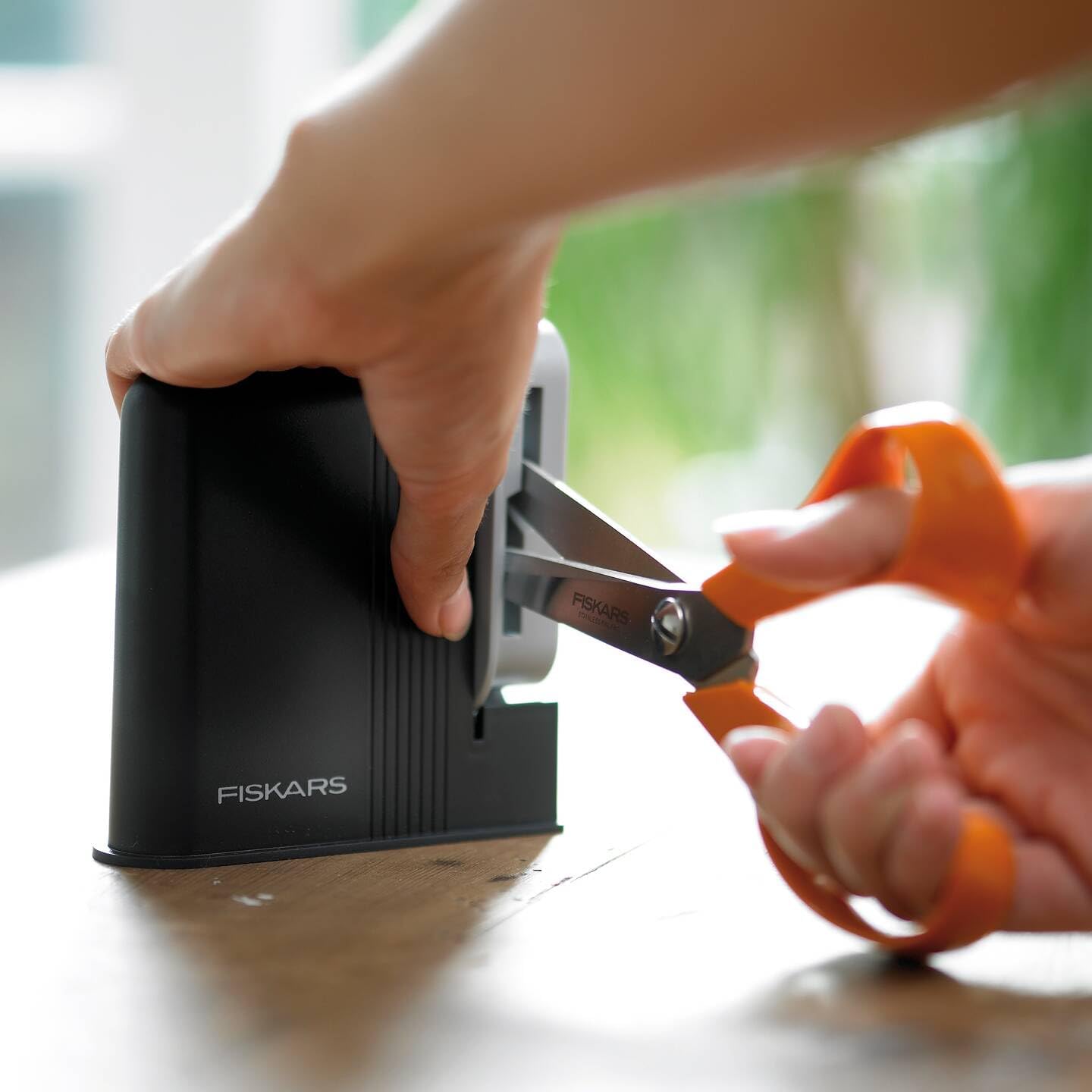 Close-up of hands using the sharpener with orange scissors