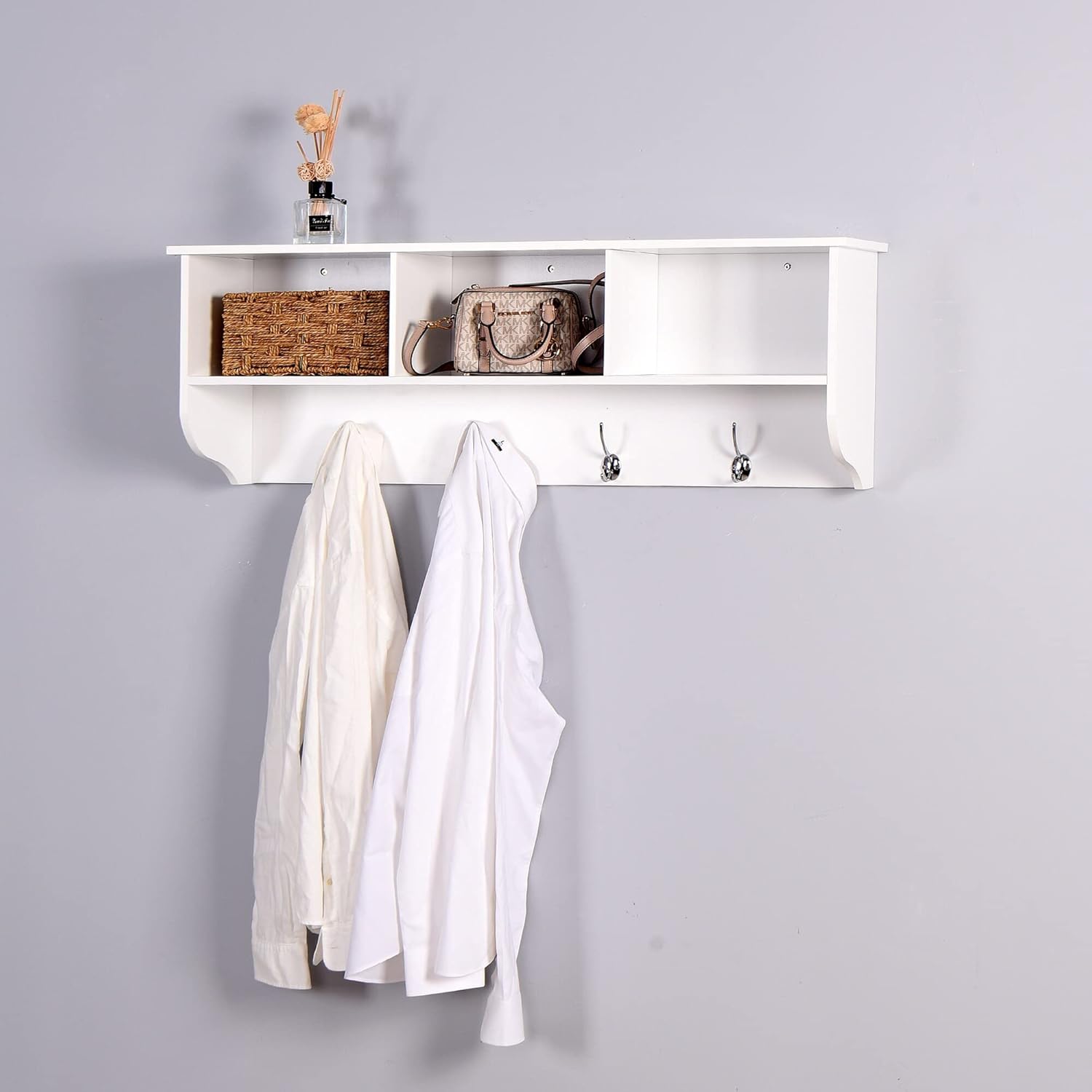 White wall-mounted coat rack installed in an entryway, displaying coats hanging on hooks and decorative items on the top shelf and in cubbies.