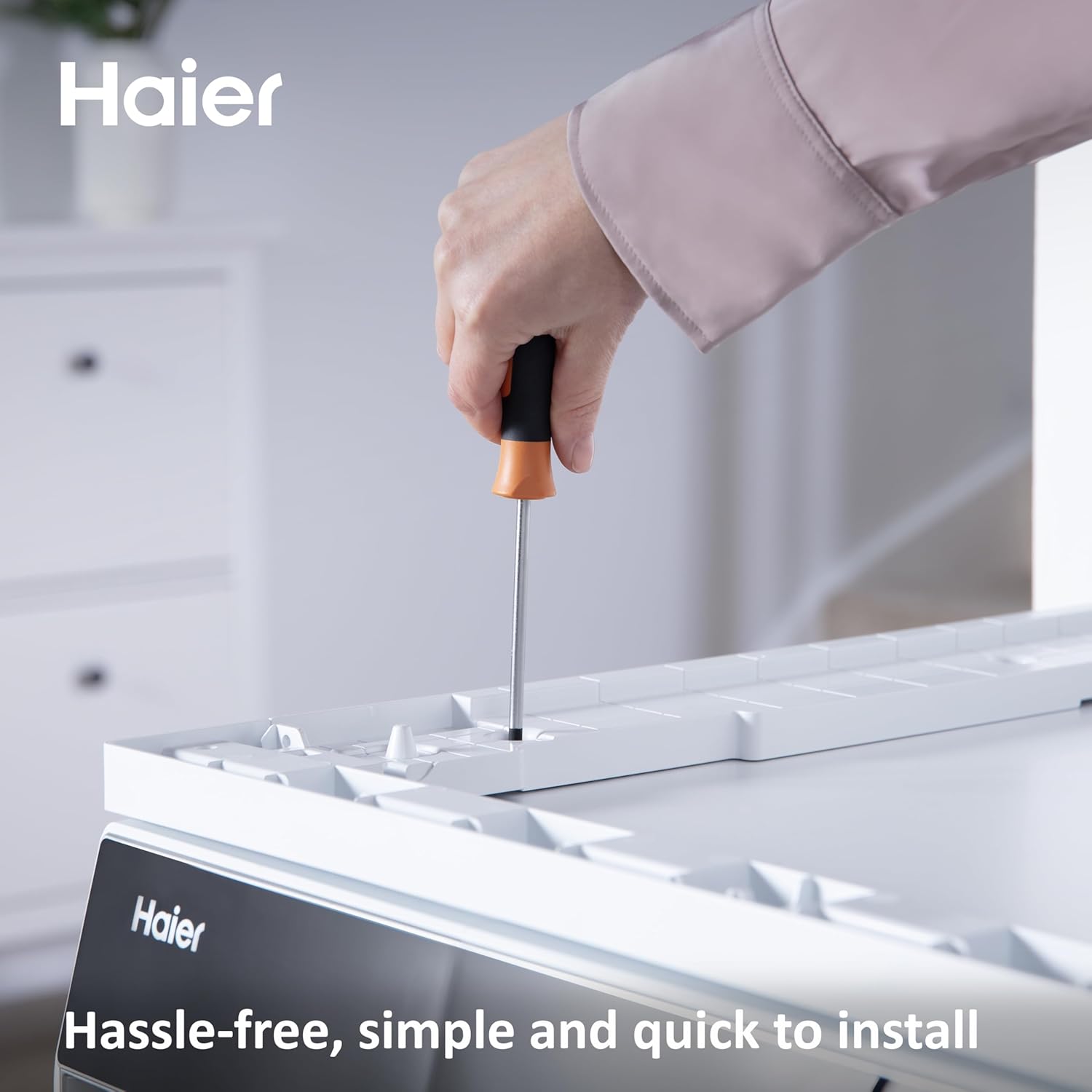 Hand using a screwdriver to secure the stacking kit to the washing machine