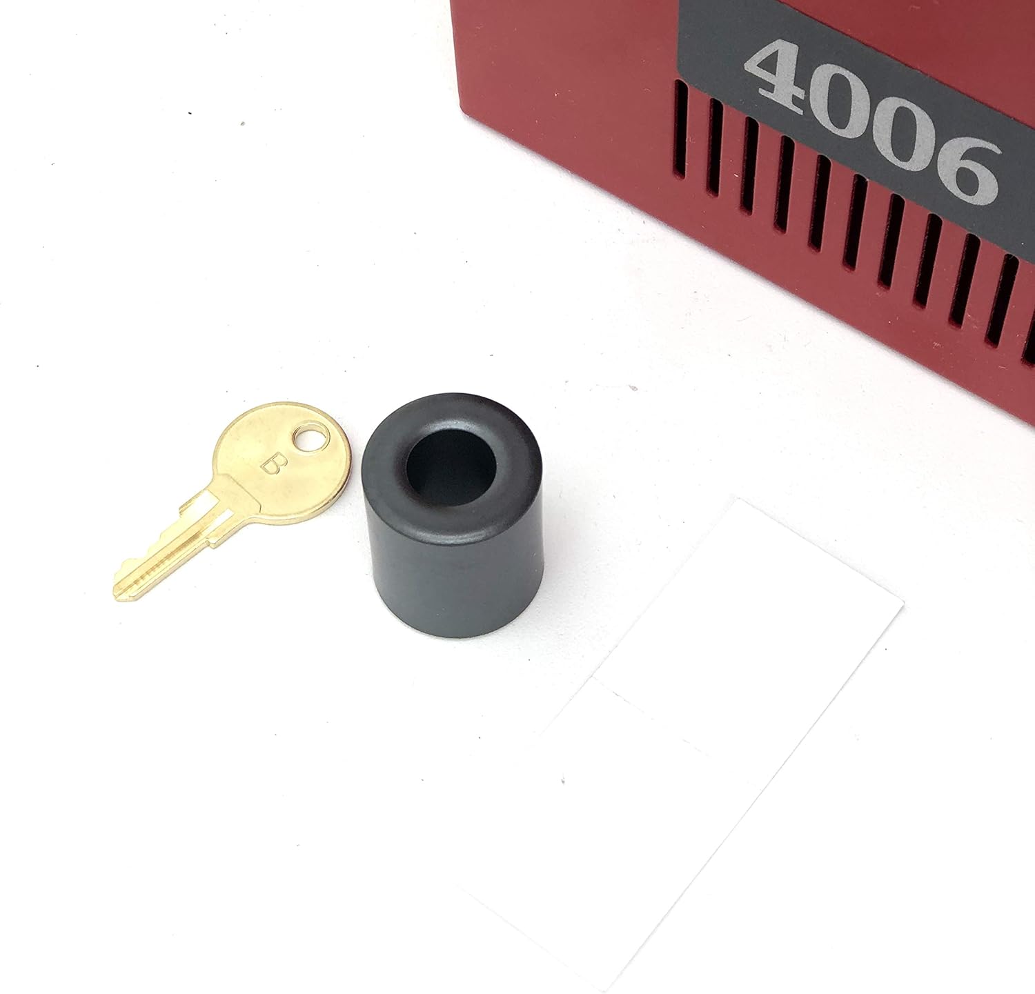 A small brass key with the letter 'B' stamped on it, next to a black cylindrical keyhole cover.