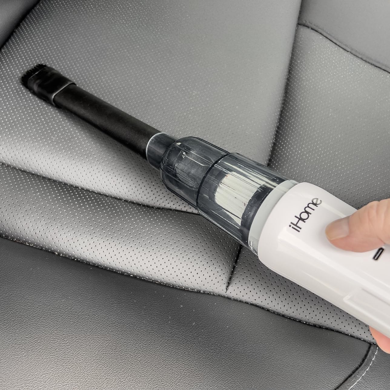 A hand holding the iHome HandVac CV15, using the crevice tool to clean between car seats.