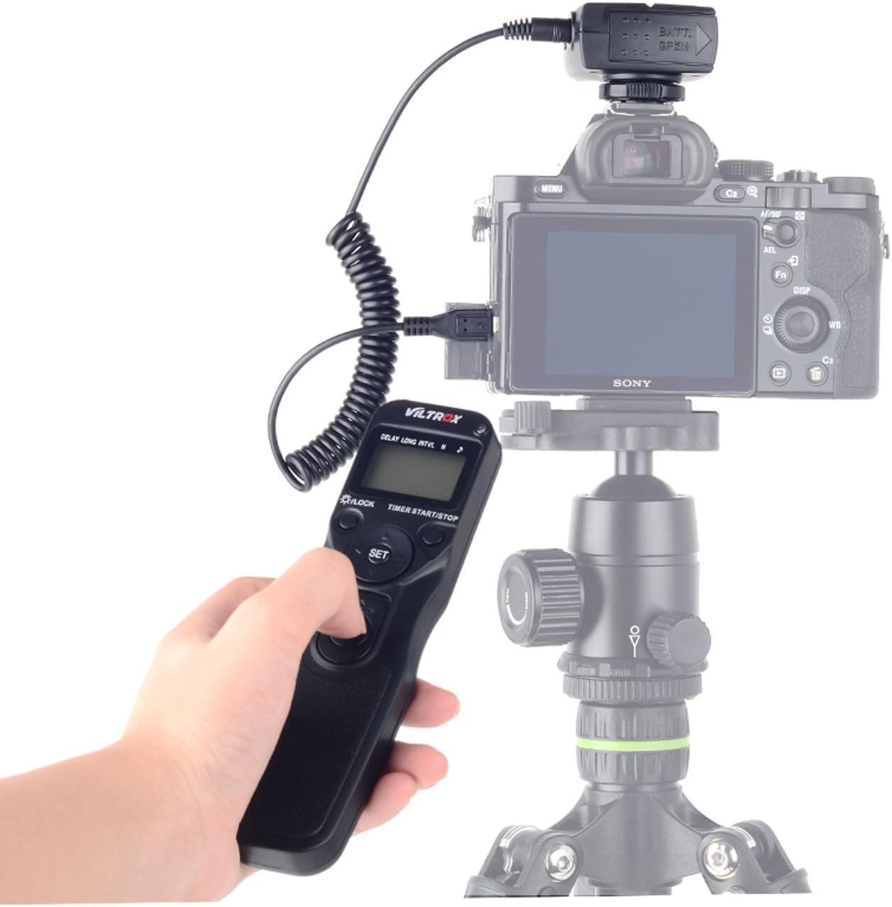 A hand holding the VILTROX JY-710-C1 transmitter, displaying timer settings on its LCD screen, with a camera and receiver in the background.