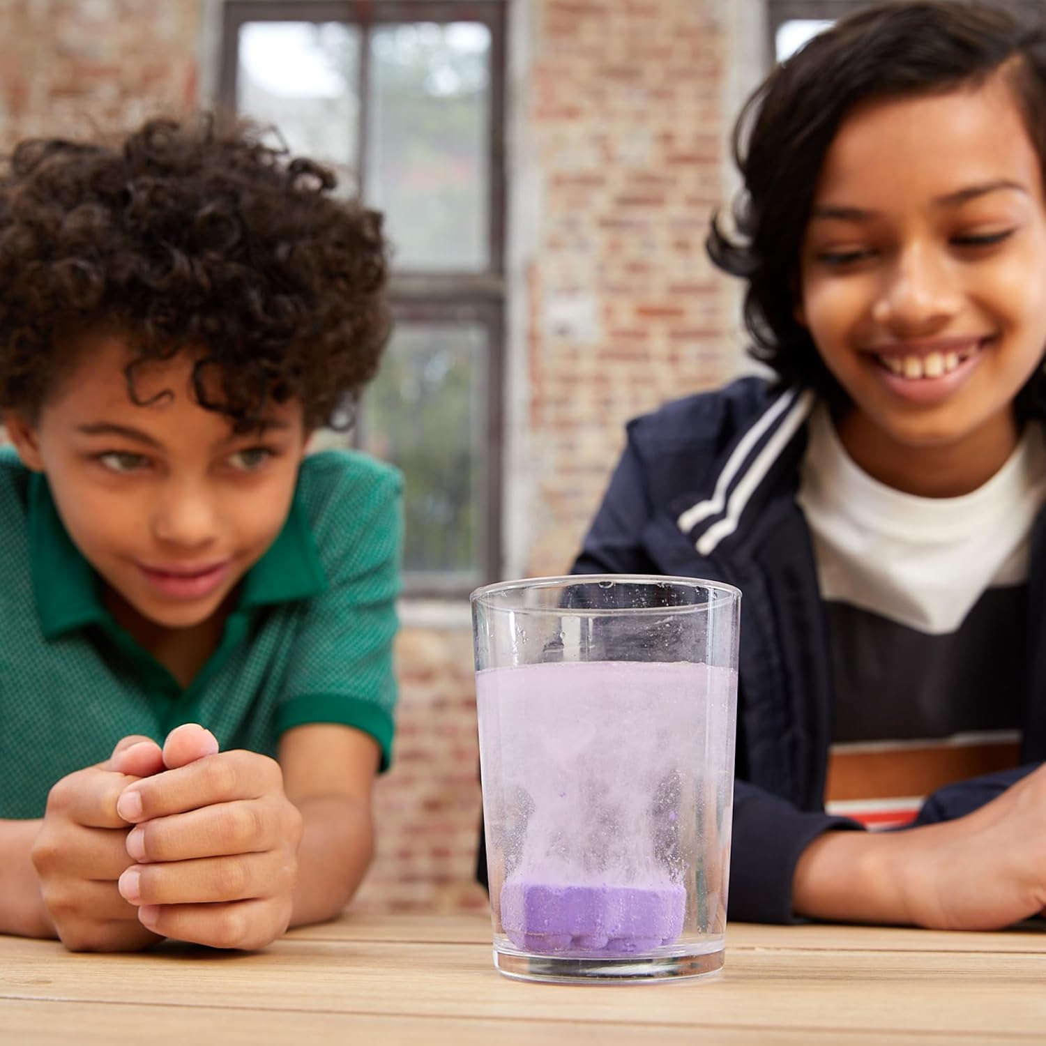 Two children observing a purple coral-like structure reacting in a glass of water.