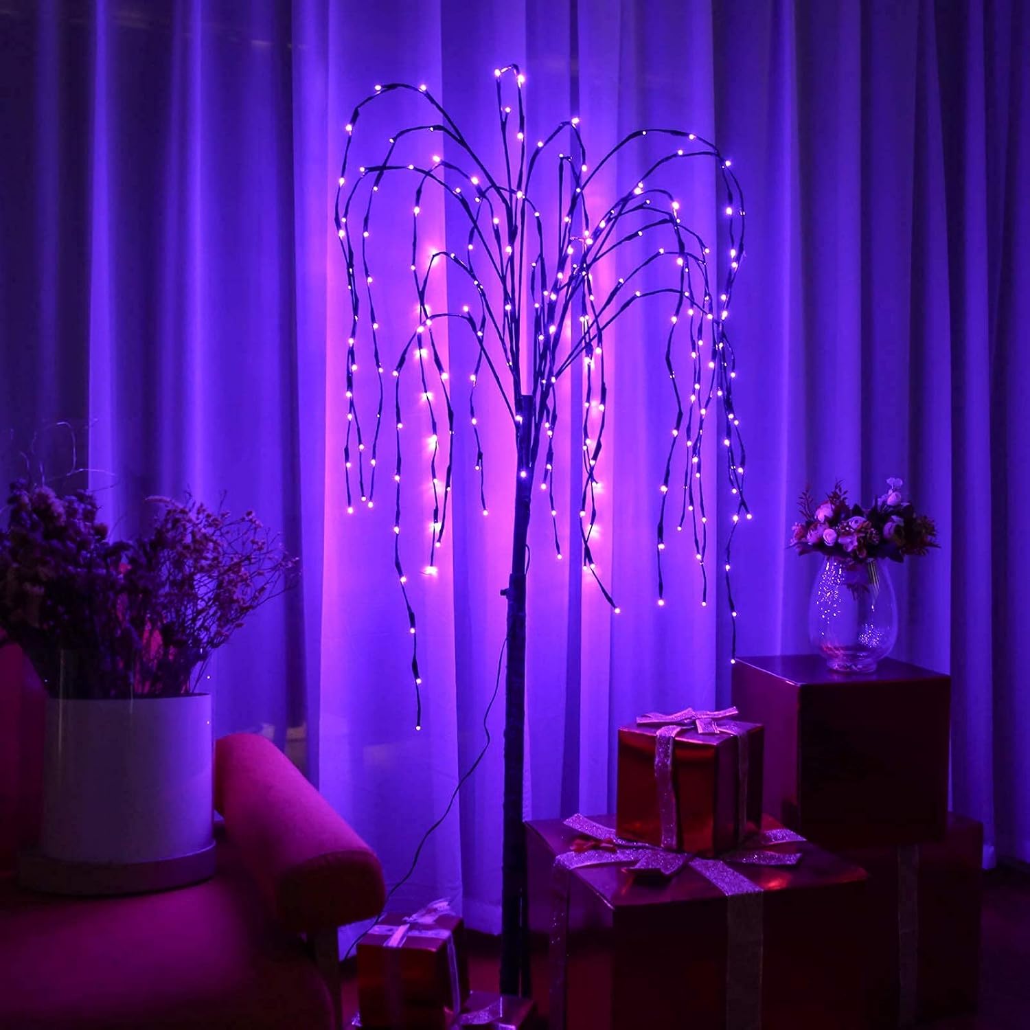 The LED Solar Willow Tree Lights with purple glow, set up indoors next to wrapped gifts, demonstrating its use as an indoor decoration.