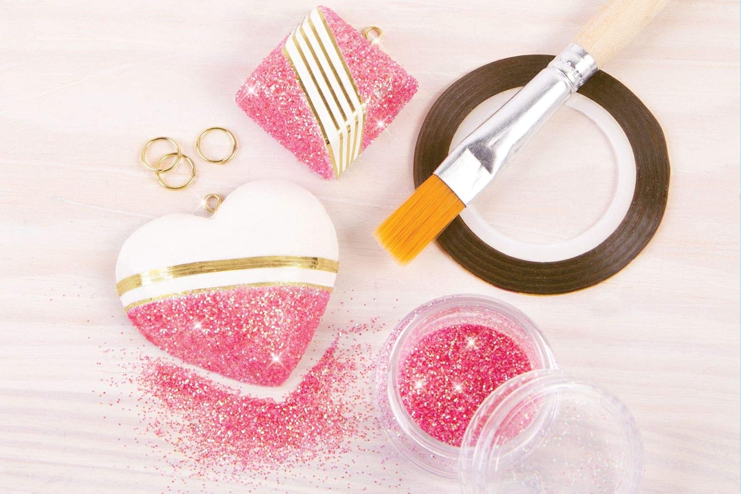 Close-up of partially decorated plaster charms, including a heart and a square shape, with pink glitter and gold metallic tape accents.
