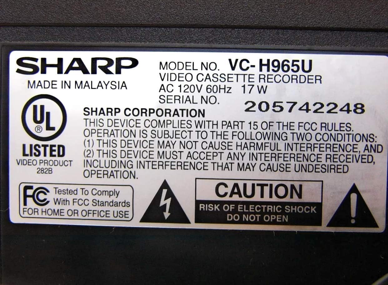 Close-up of the Sharp VC-H965U product label showing model number, serial number, power requirements, and safety warnings including 'CAUTION RISK OF ELECTRIC SHOCK DO NOT OPEN'.