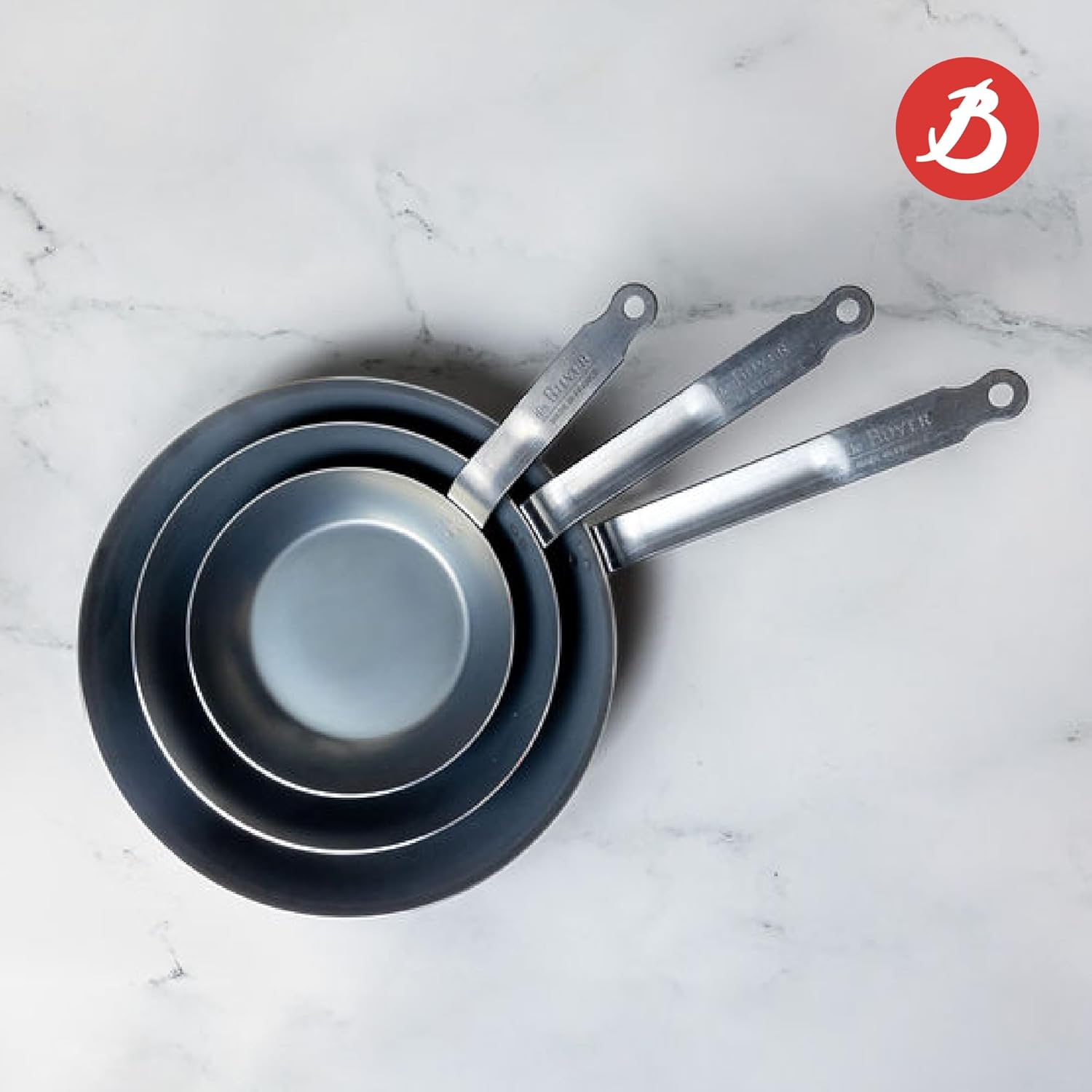 Three De Buyer Fry Pans Stacked on a Marble Surface