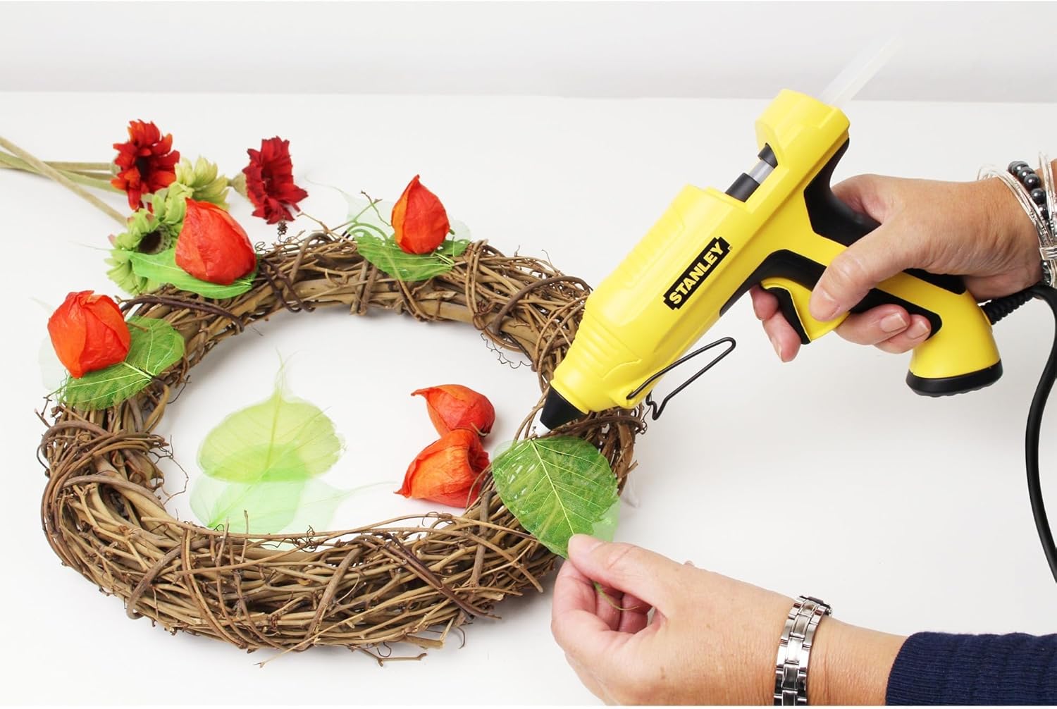 A person using the Stanley STHT6-70417 glue gun to attach a green leaf to a decorative wreath made of twigs.