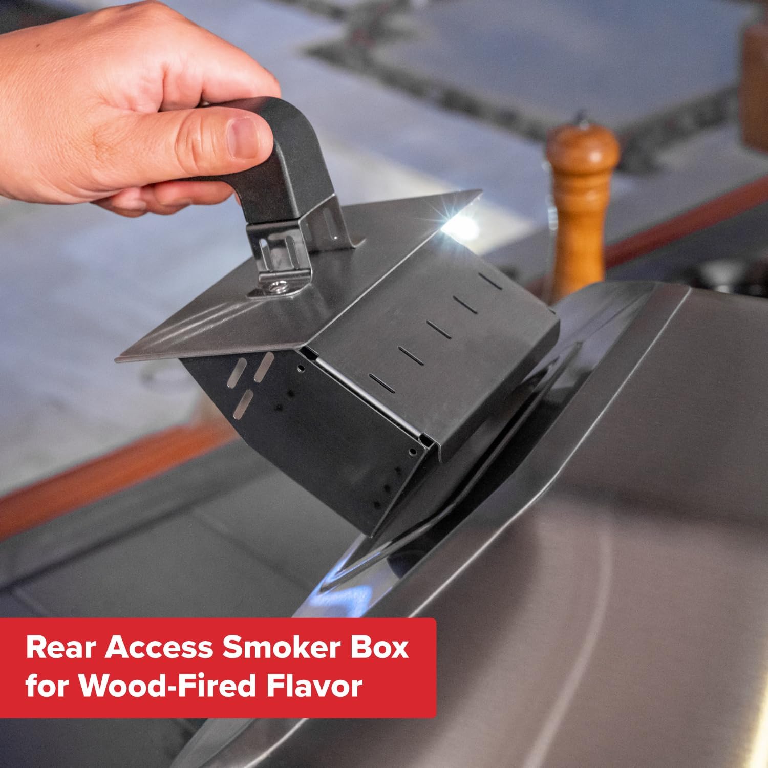 Hand placing wood chips into the rear access smoker box of the Nexgrill pizza oven