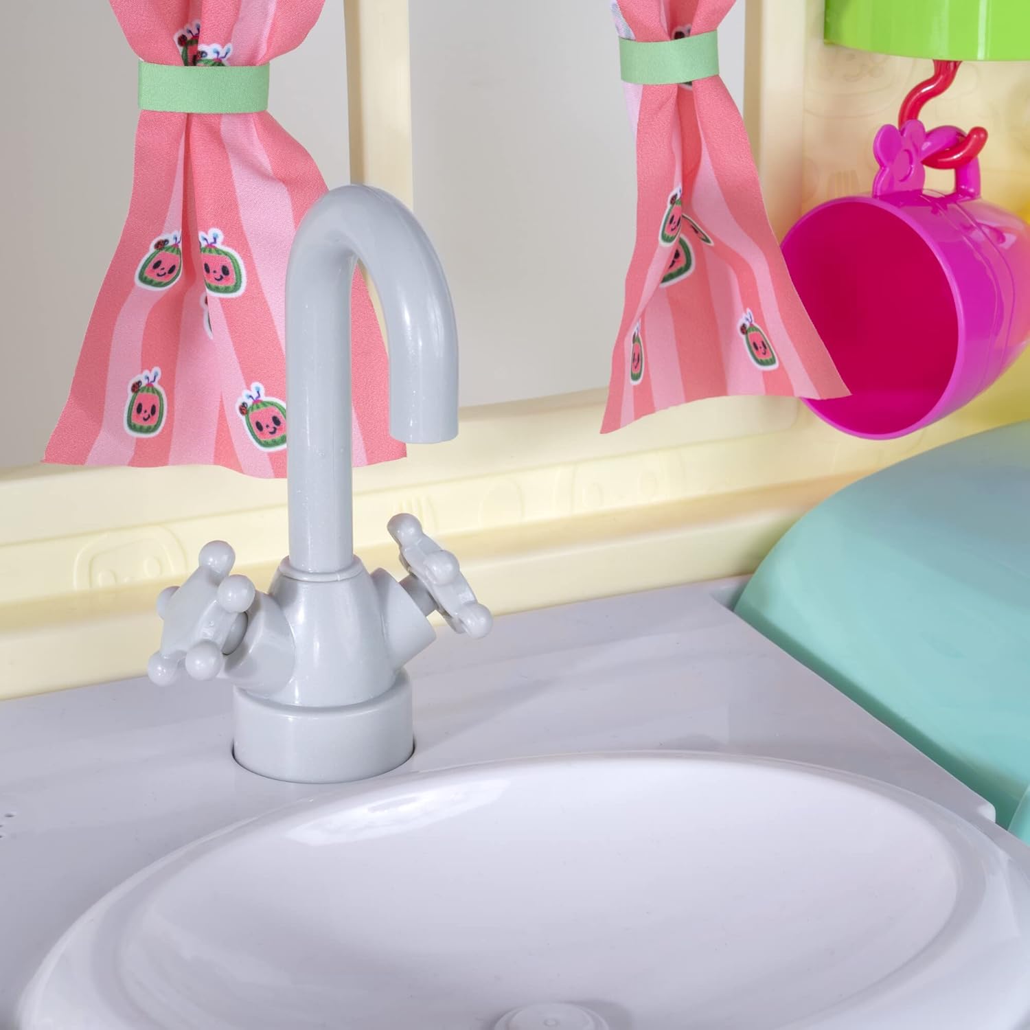 Close-up of the CoComelon kitchen sink with a grey faucet and pink curtains in the background.