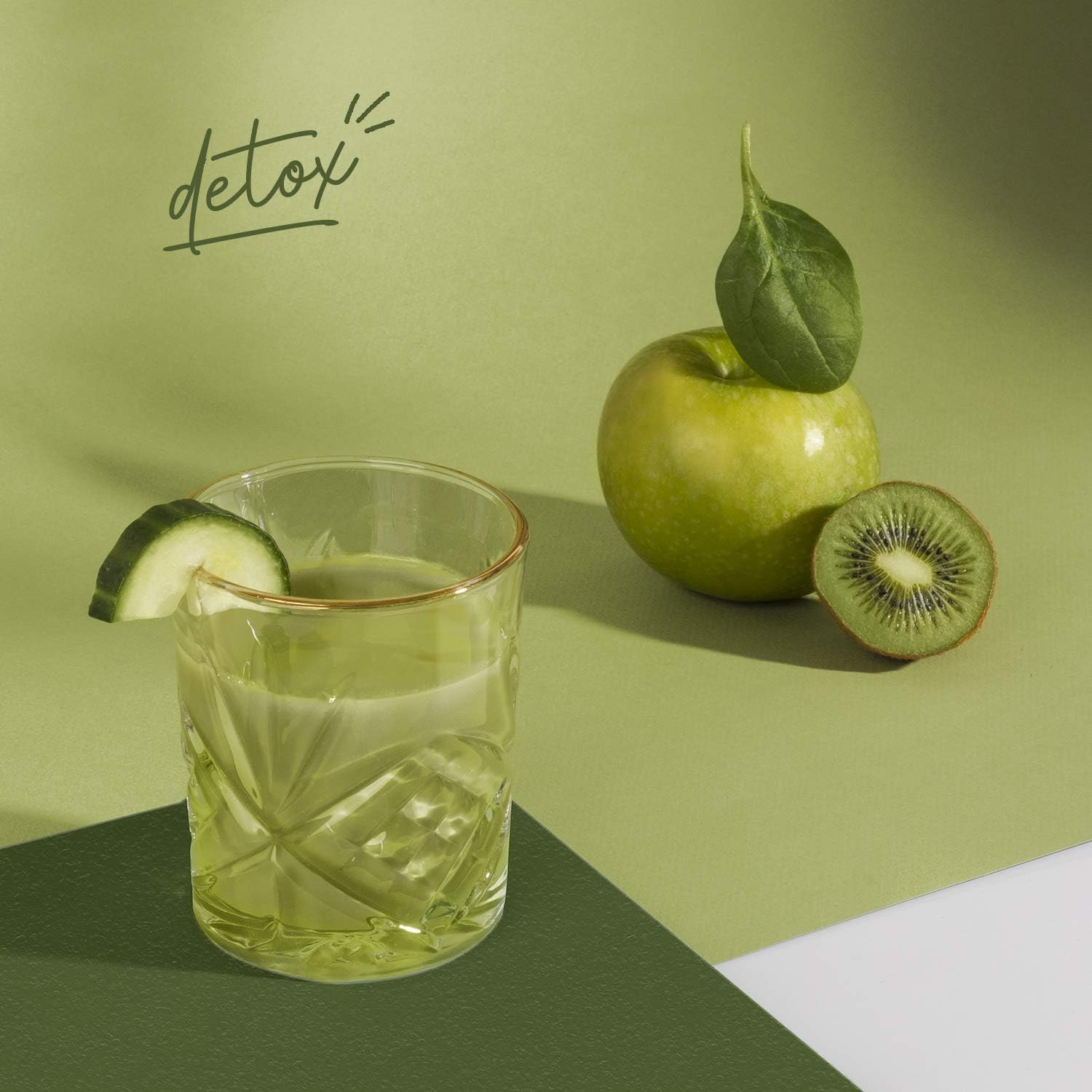 A refreshing green smoothie in a glass, garnished with a cucumber slice, alongside a green apple and half a kiwi.