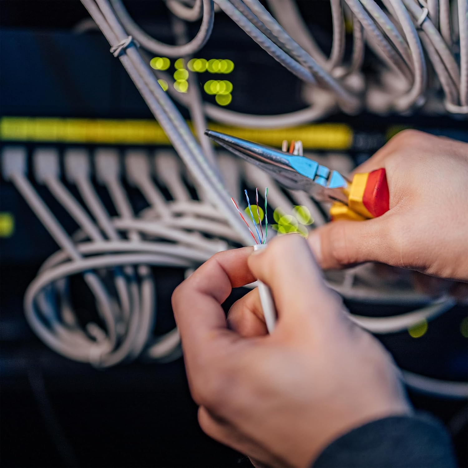 Hands using a crimping tool to attach an RJ45 connector to a Cat5e cable, securing the wires.