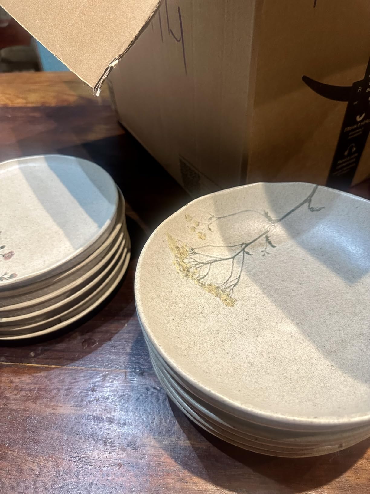Pilha de pratos de sobremesa Porto Brasil Bio Stoneware com detalhe em relevo e estampa floral ao lado de caixa de entrega