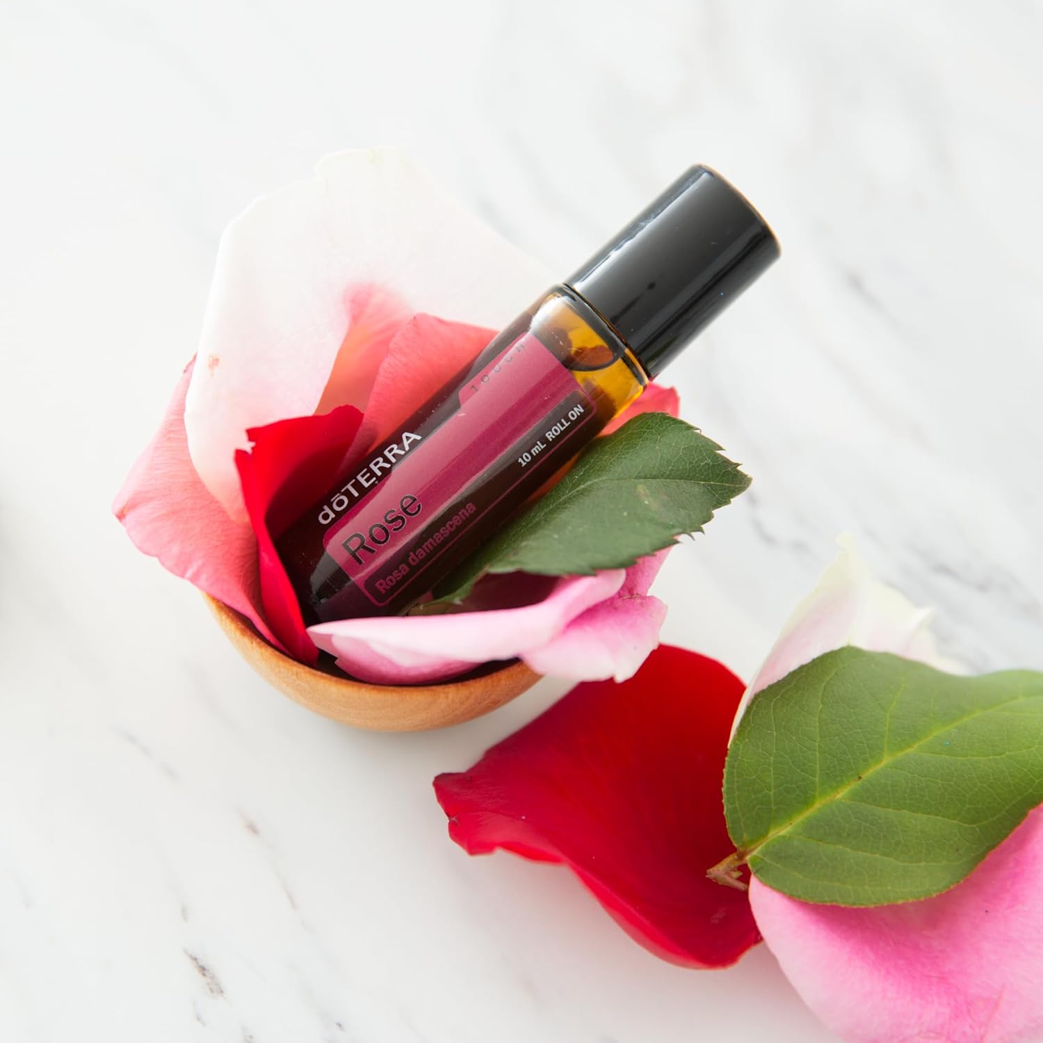 doTERRA Rose Touch essential oil bottle surrounded by fresh rose petals.