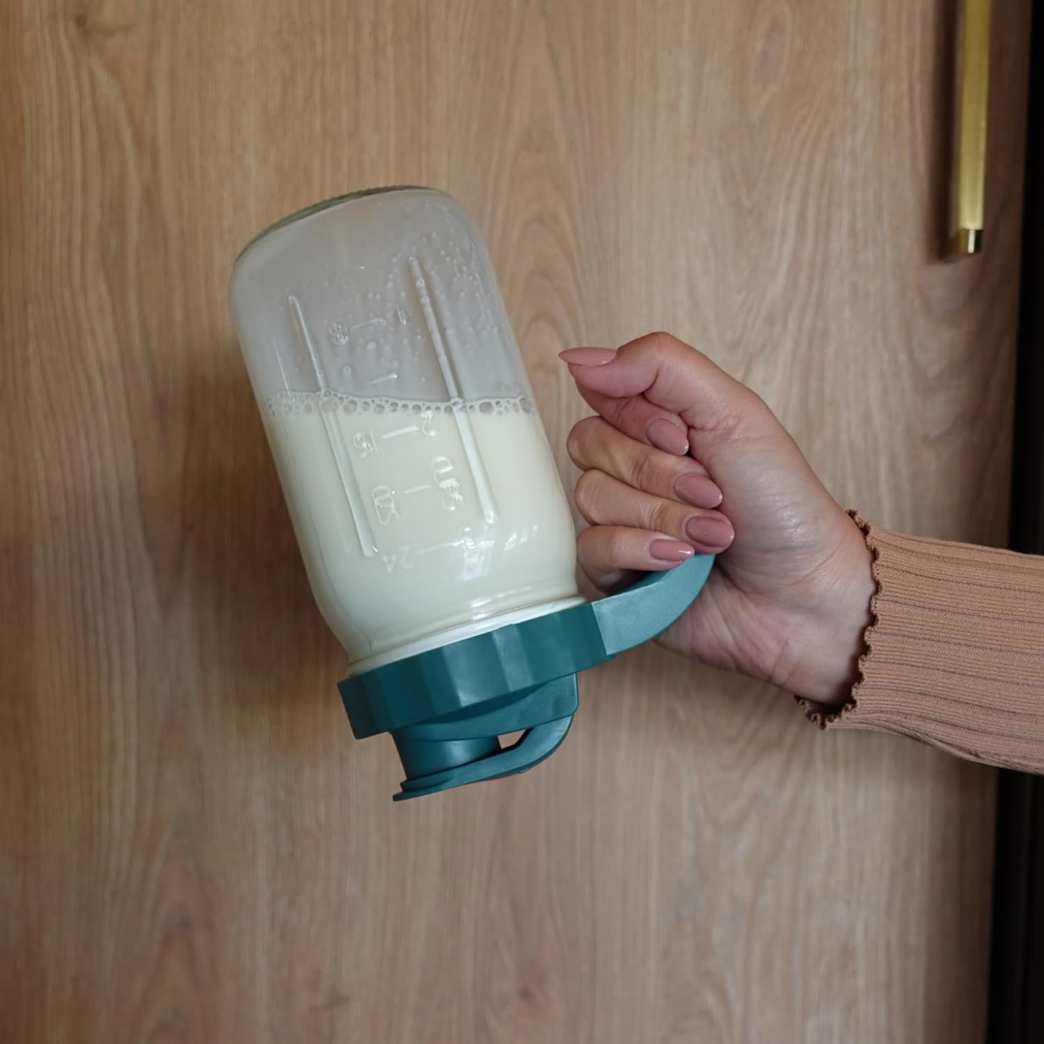 Hand holding the Willow pitcher with milk, demonstrating its ergonomic handle
