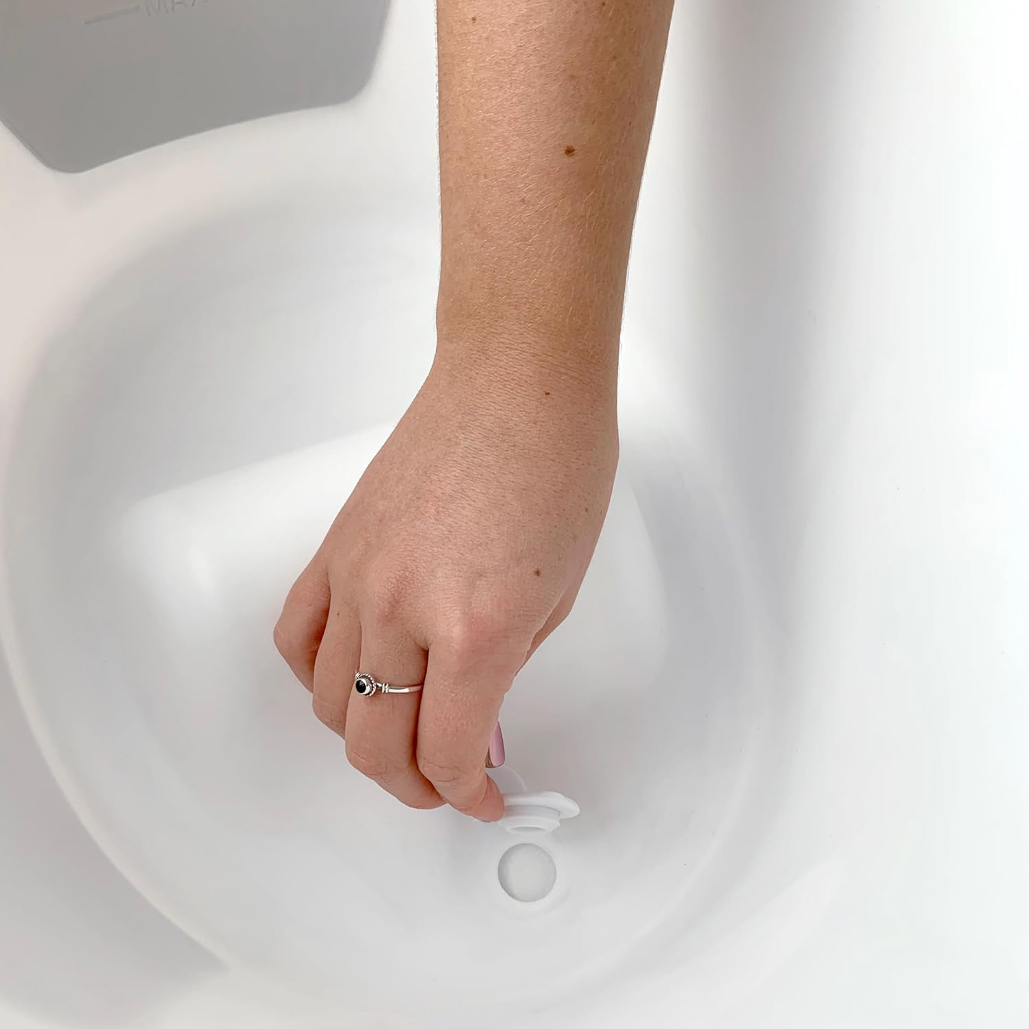 Hand removing drain plug from SHNUGGLE bath
