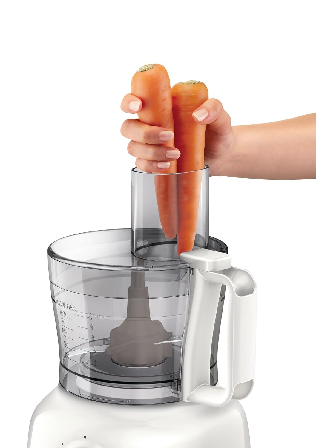 A hand inserting two carrots into the feeder tube of the food processor.