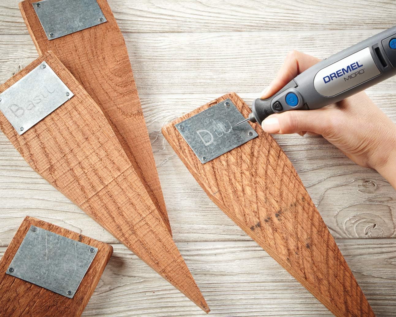 Hand using Dremel Micro to engrave a metal plate on a wooden stake