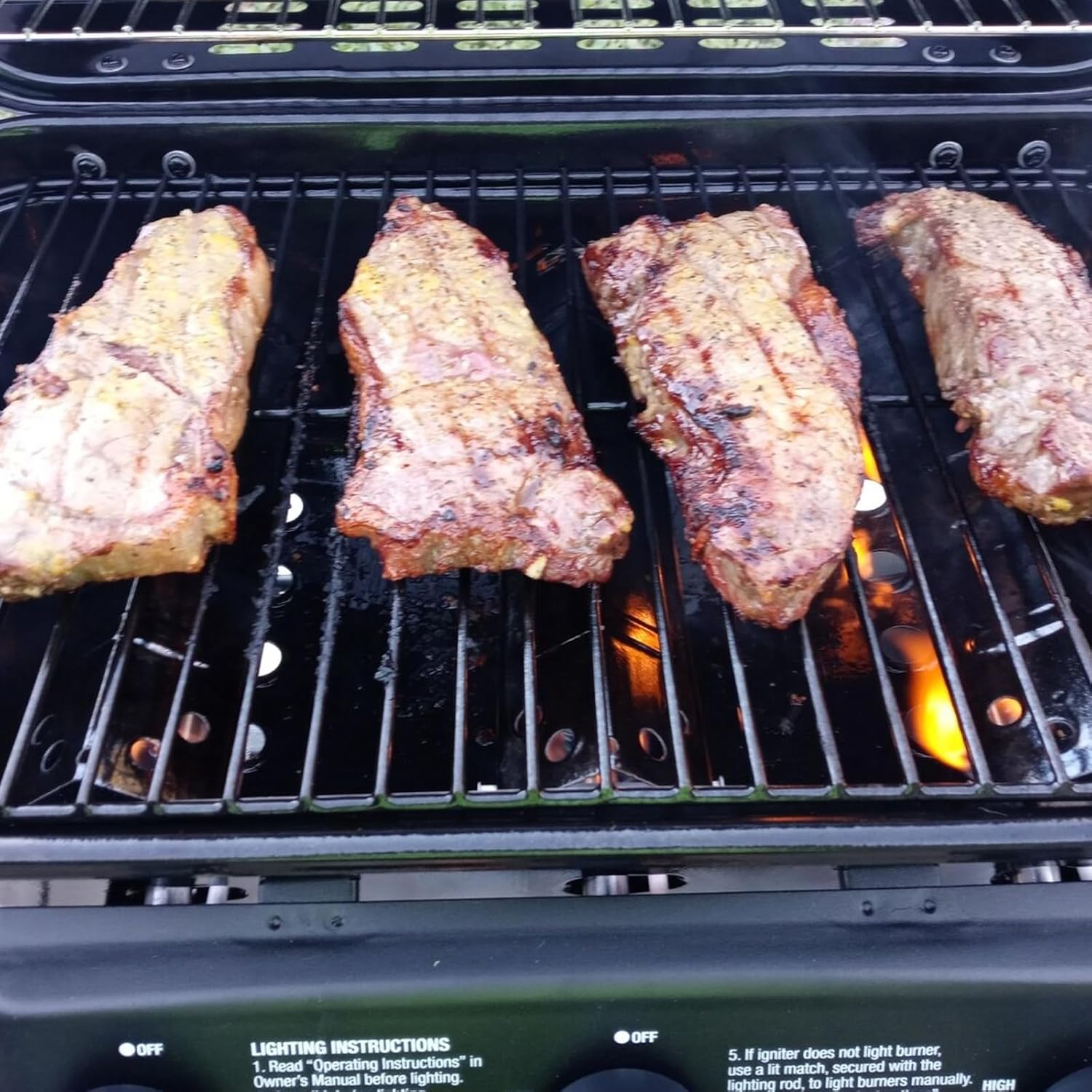 Steaks cooking on a grill with visible flames and heat plates below the grates