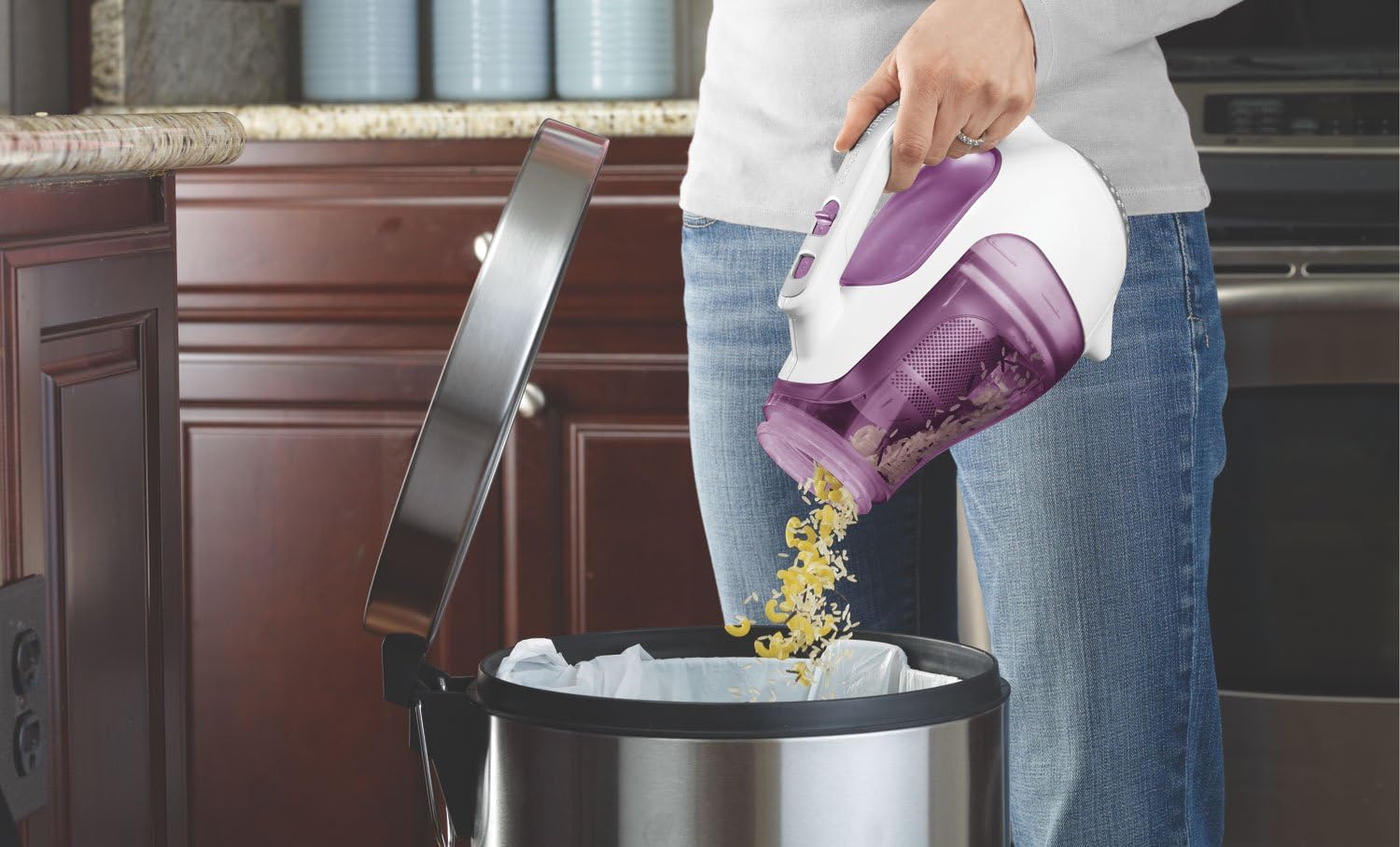 Person emptying the translucent dirt bowl of the BLACK+DECKER CHV1210 Dustbuster into a trash can.