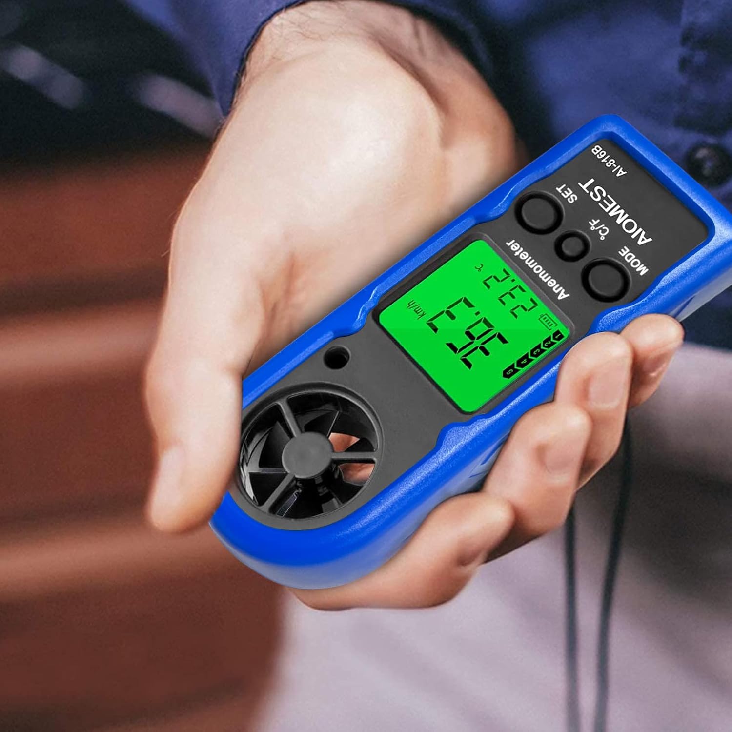 A hand holding the AIOMEST Digital Anemometer AI-816B, showing a wind speed reading of 36.7 km/h and a temperature of 23.2°C on its backlit display.