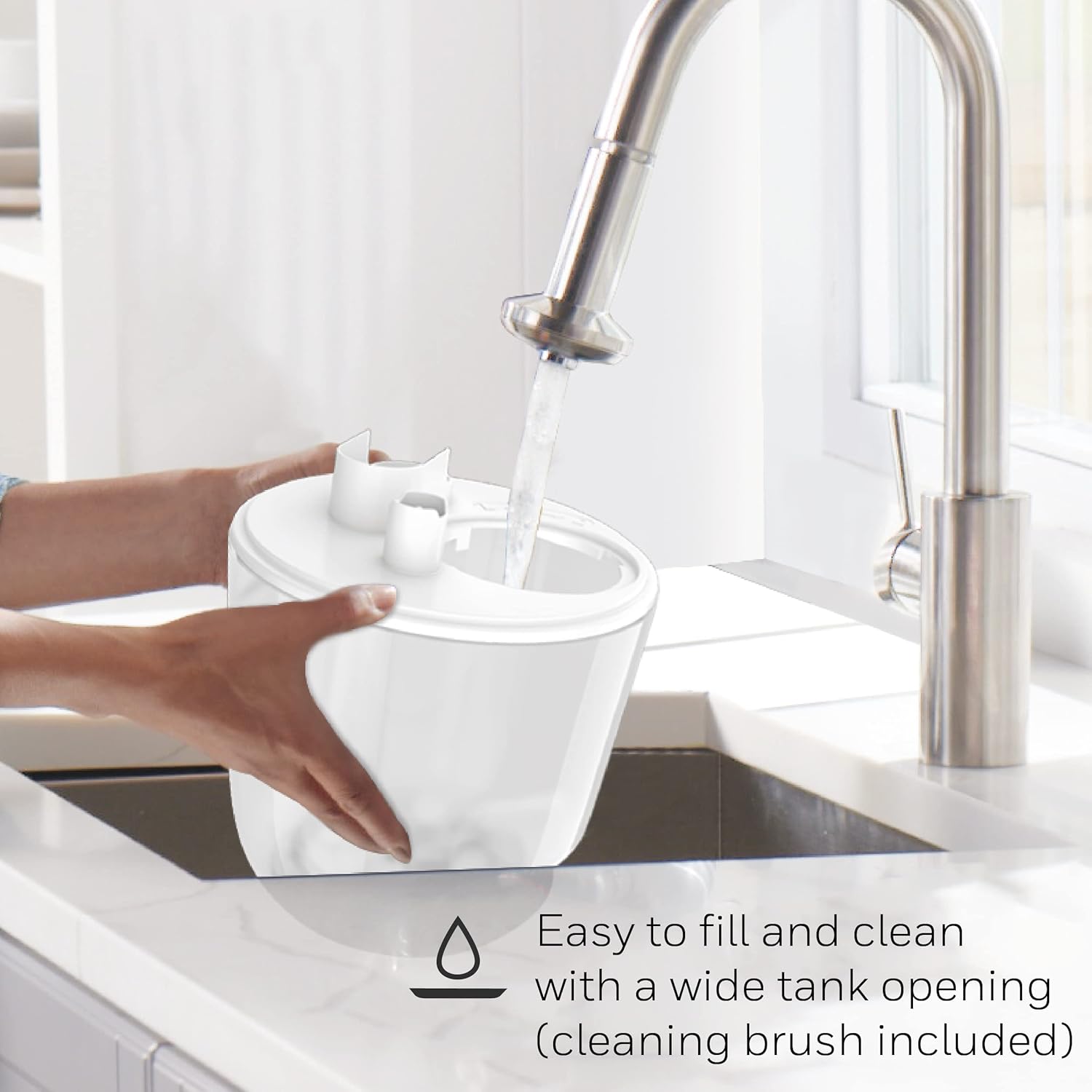 Hands filling the Honeywell humidifier water tank under a kitchen faucet, demonstrating the wide tank opening for easy refilling.
