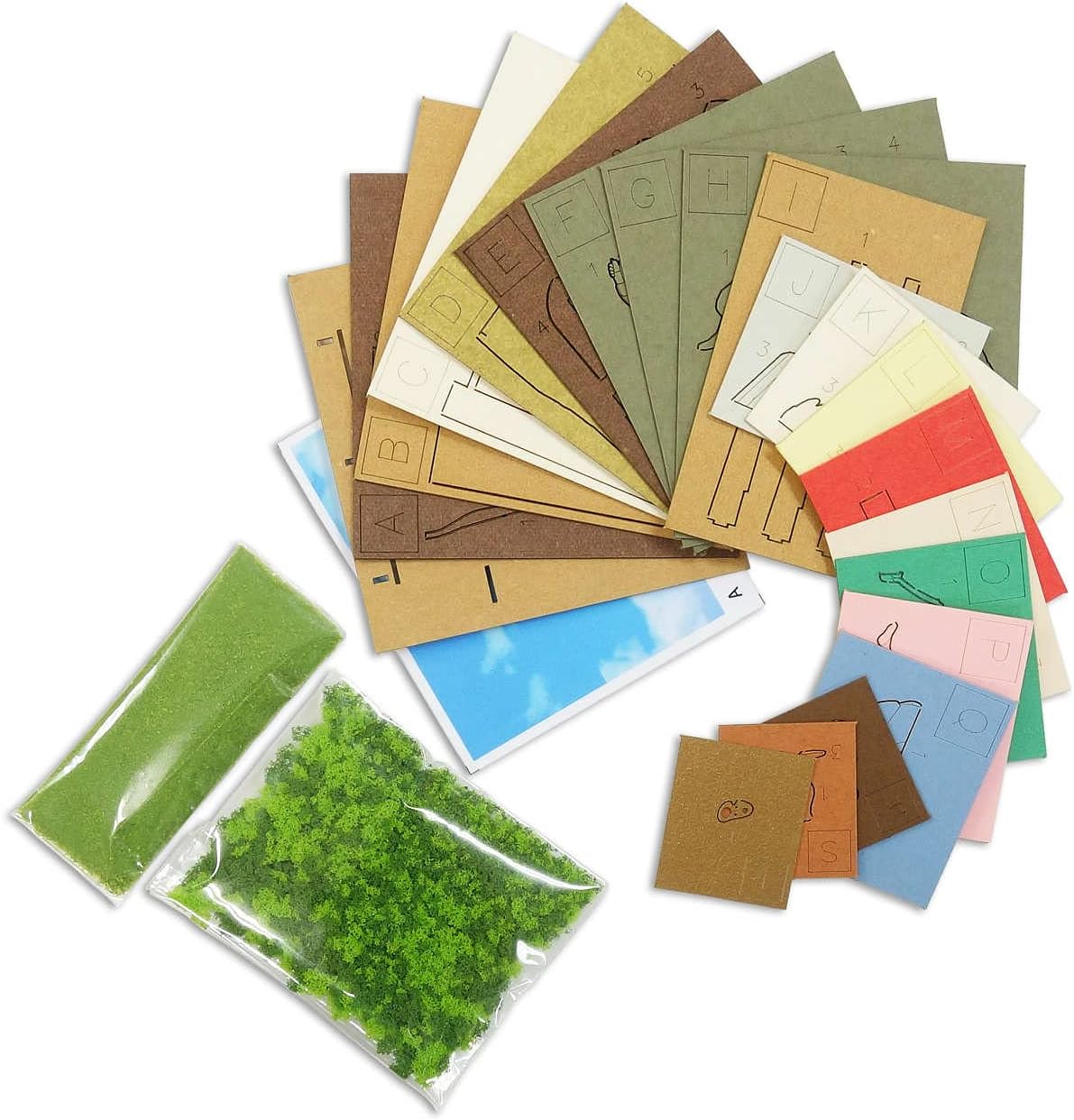 Various colored laser-cut paper sheets and bags of green flocking material, representing the kit components.