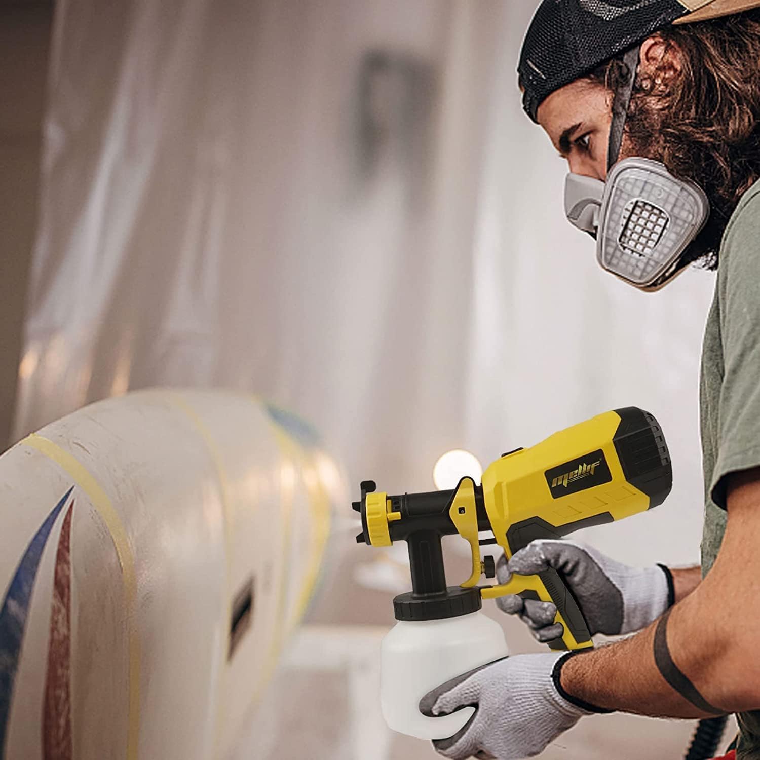 A person wearing a respirator and gloves using the Mellif paint sprayer to paint a curved surface, demonstrating precise application.